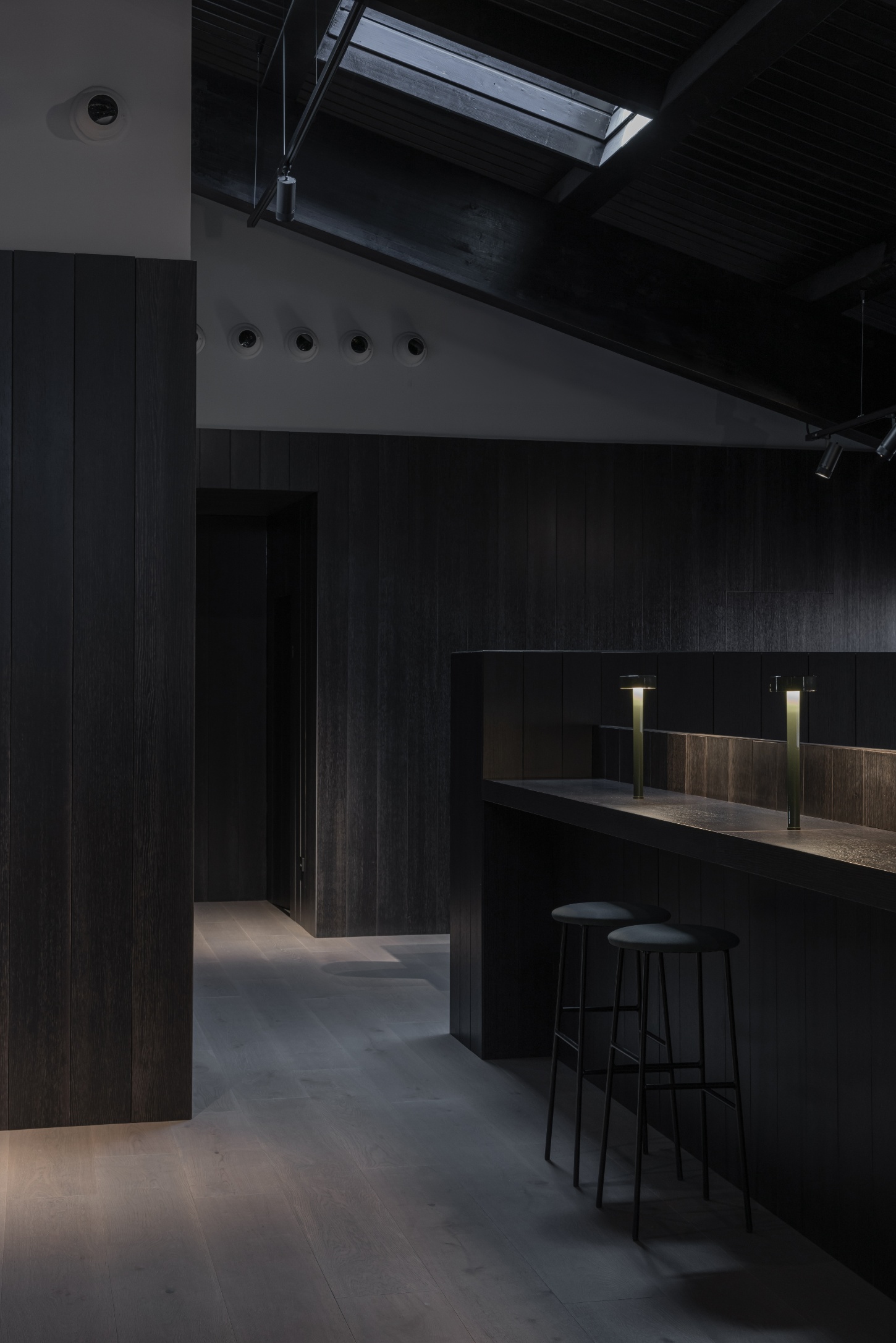 Tritium Winery by Francesc Rifé Studio — The interior tasting space of Tritium Winery features a minimalist bar configuration anchored by charred timber wall paneling that extends vertically from...