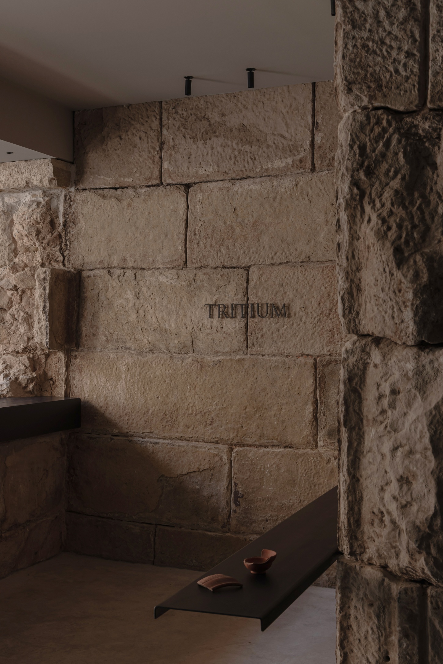 Tritium Winery by Francesc Rifé Studio — A close-up view of the 15th-century stone structure's interior reveals precisely coursed ashlar blocks with 'TRITIUM' carved into a central stone.