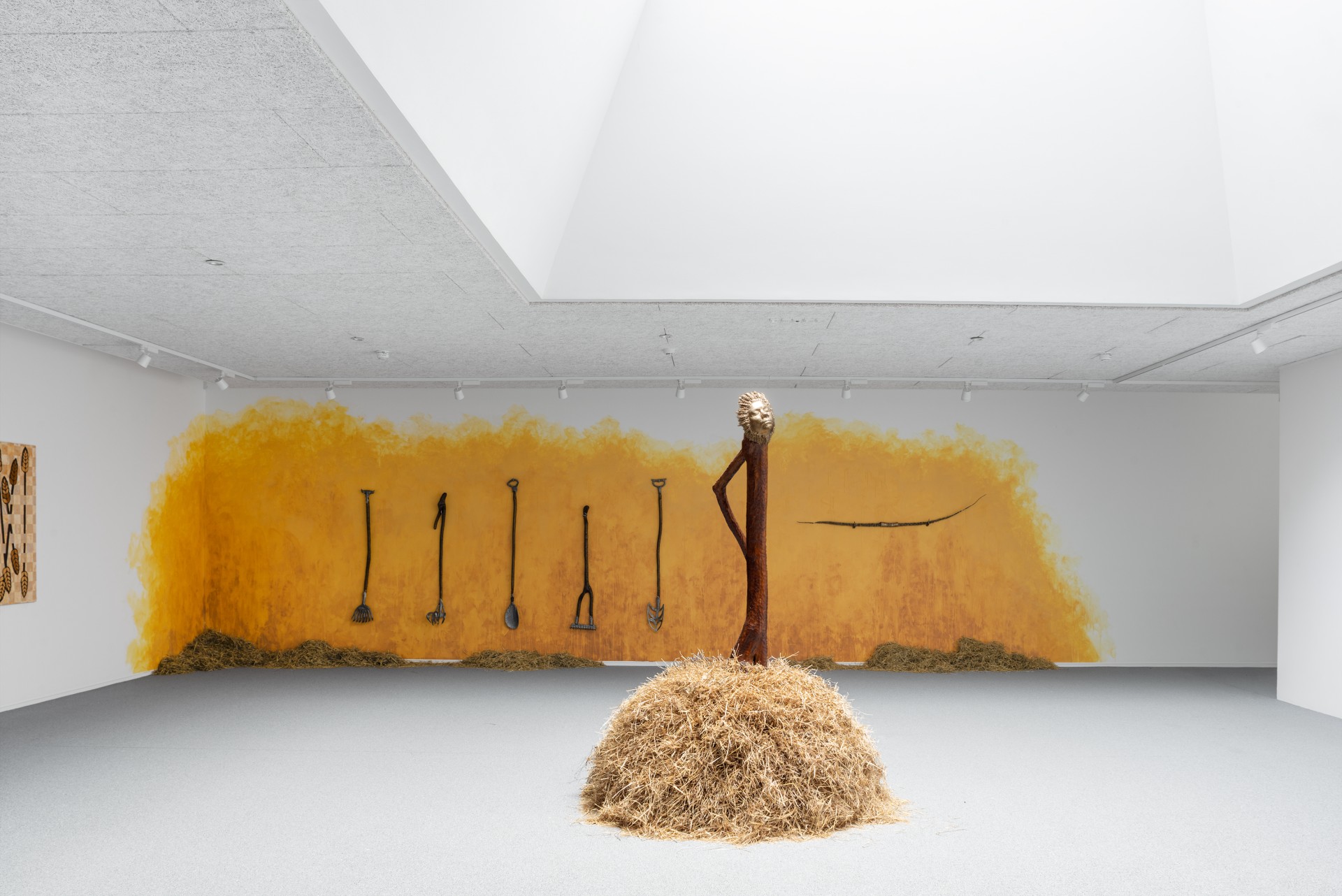 Bleak Harvest by Anna Bak at Vestjyllands Kunstpavillon — A wooden sculptural figure dominates the gallery floor, its contorted body constructed from timber with an elongated, curved form suggesting physical strain.