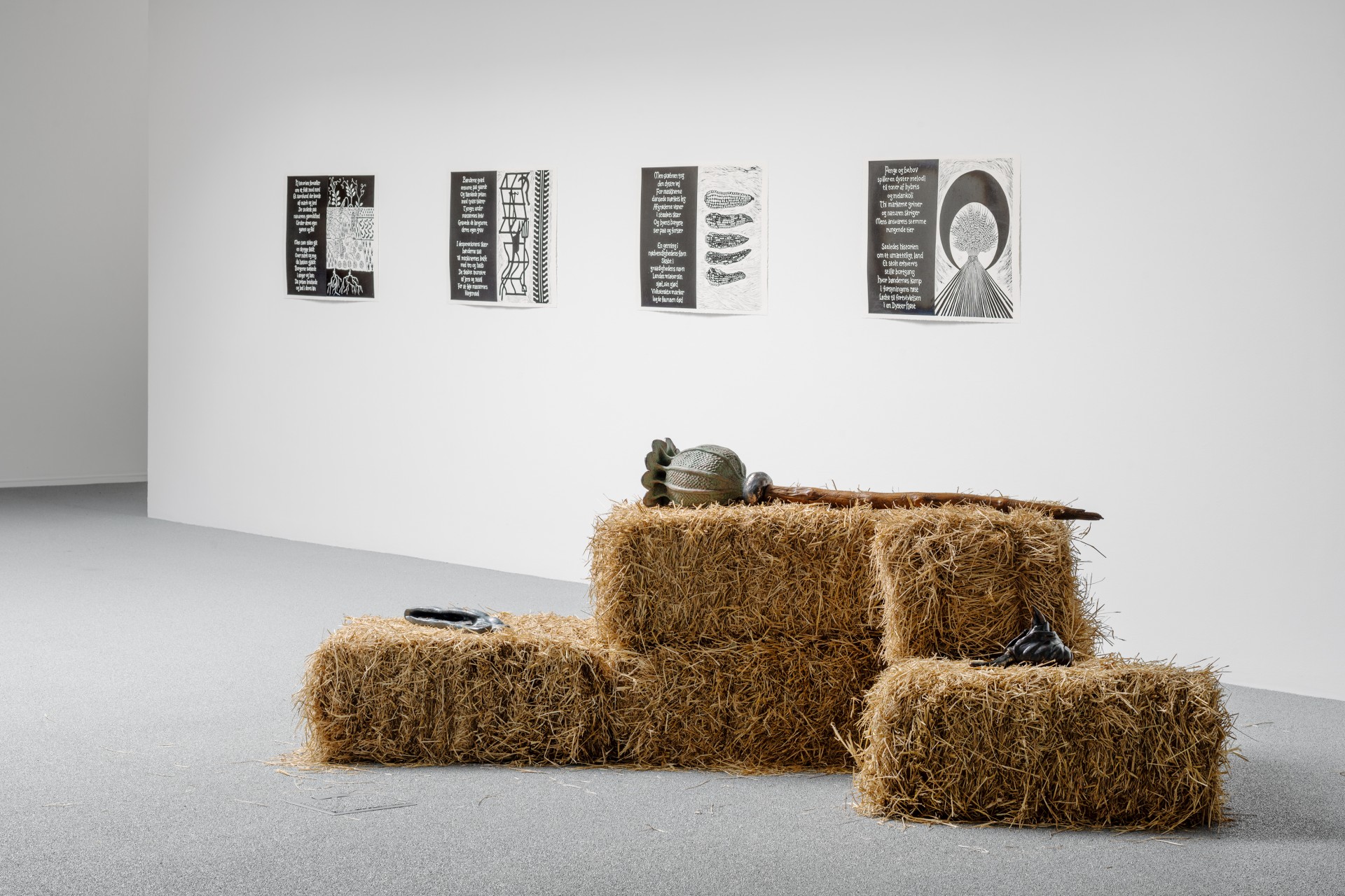 Bleak Harvest by Anna Bak at Vestjyllands Kunstpavillon — A wooden sculptural figure with an elongated, contorted form rises from a massive foundation of loose straw.