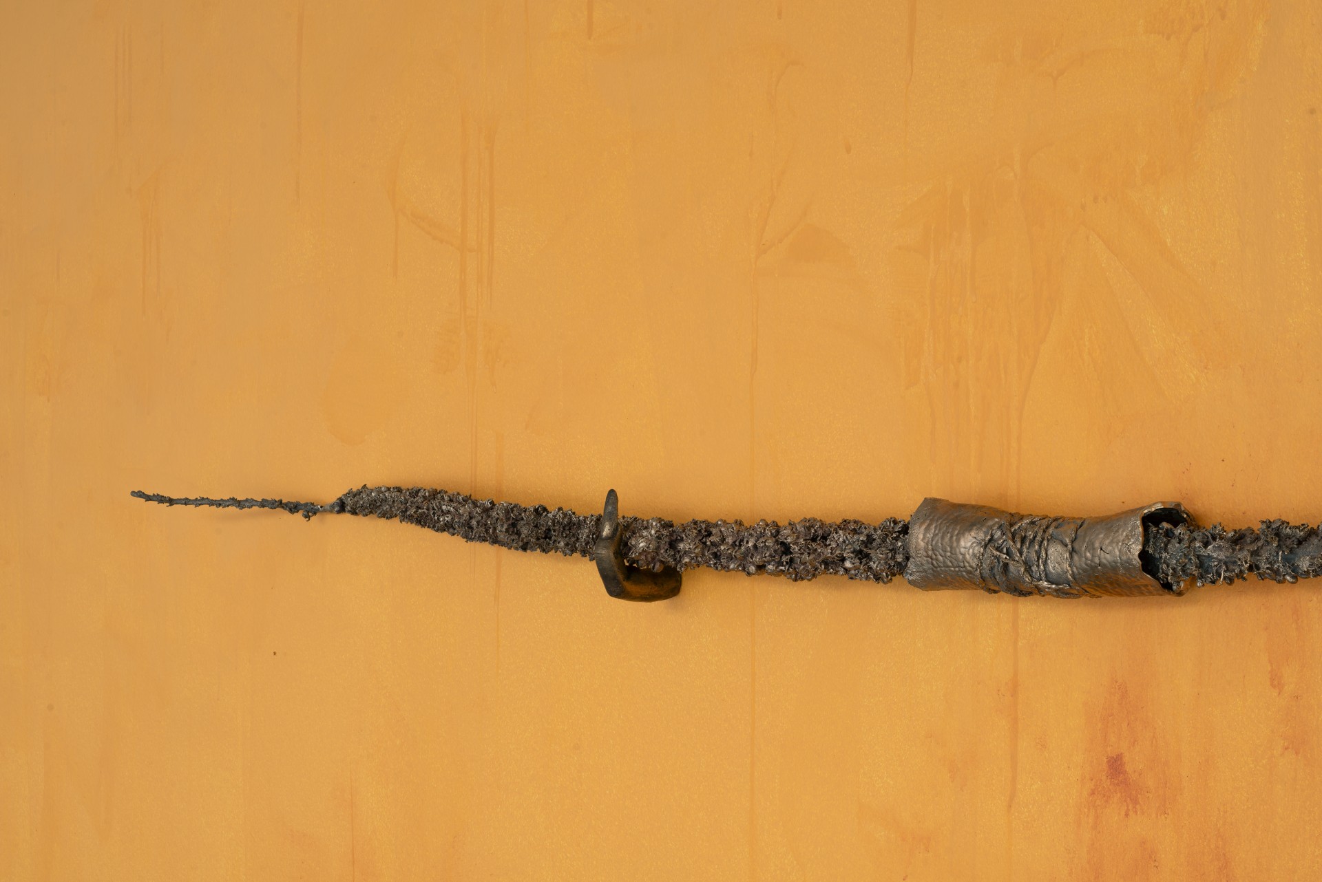 Bleak Harvest by Anna Bak at Vestjyllands Kunstpavillon — A sculptural assemblage mounted horizontally against an ochre-rendered wall.