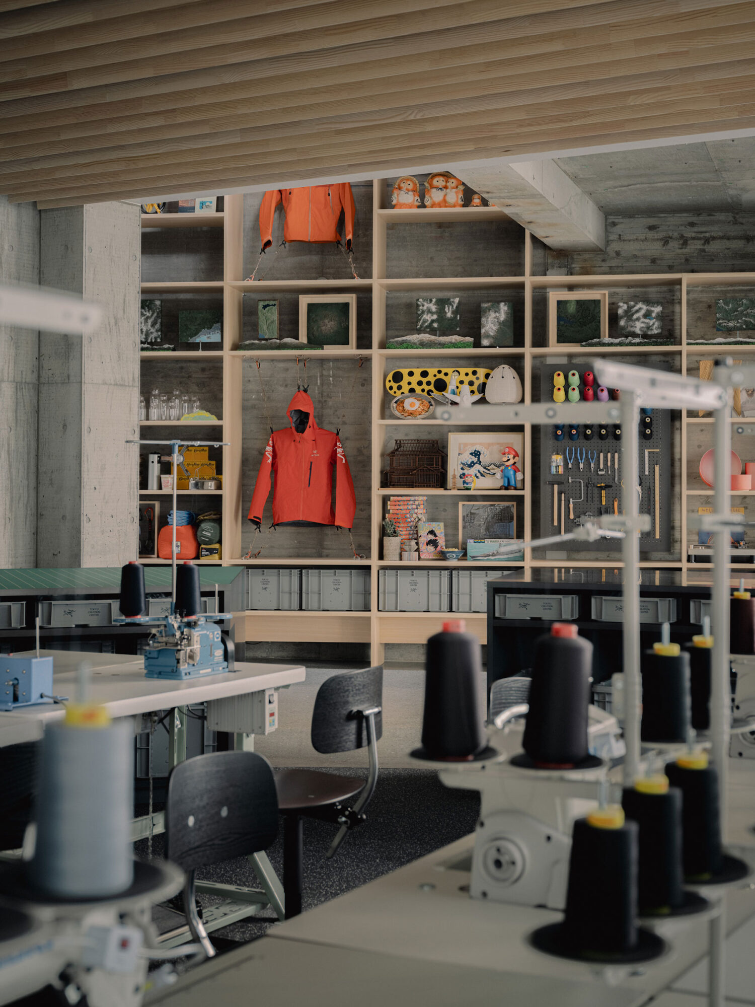 Arc’teryx Tokyo Creation Center by Torafu Architects — A deep-focus photograph captures the Arc'teryx Tokyo Creation Center's interior workspace, where shelving units in light timber dominate the background wall.