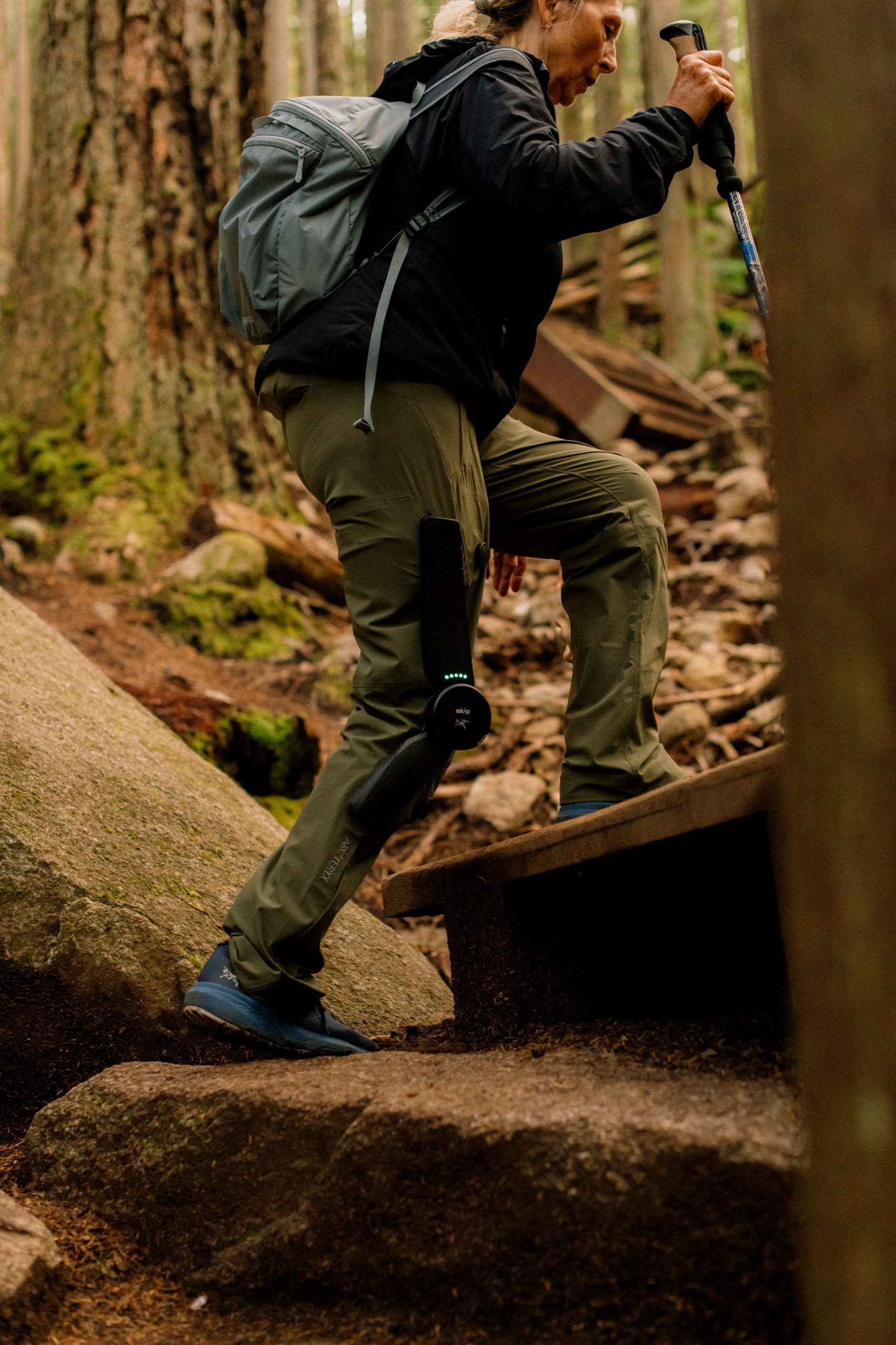 MO/GO Pants with Exoskeleton by Arc'teryx + Skip — A hiker navigates a narrow forest passage wearing Arc'teryx MO/GO pants equipped with an integrated exoskeleton system.