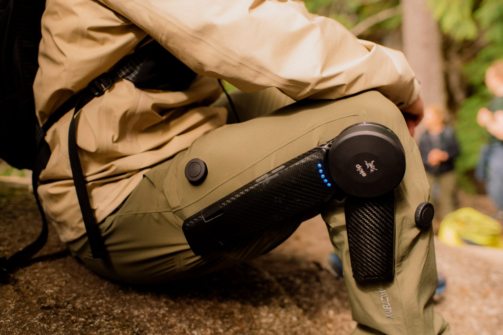 MO/GO Pants with Exoskeleton by Arc'teryx + Skip — A close-up low-angle photograph of the motorized exoskeleton system integrated into tan ripstop hiking trousers.