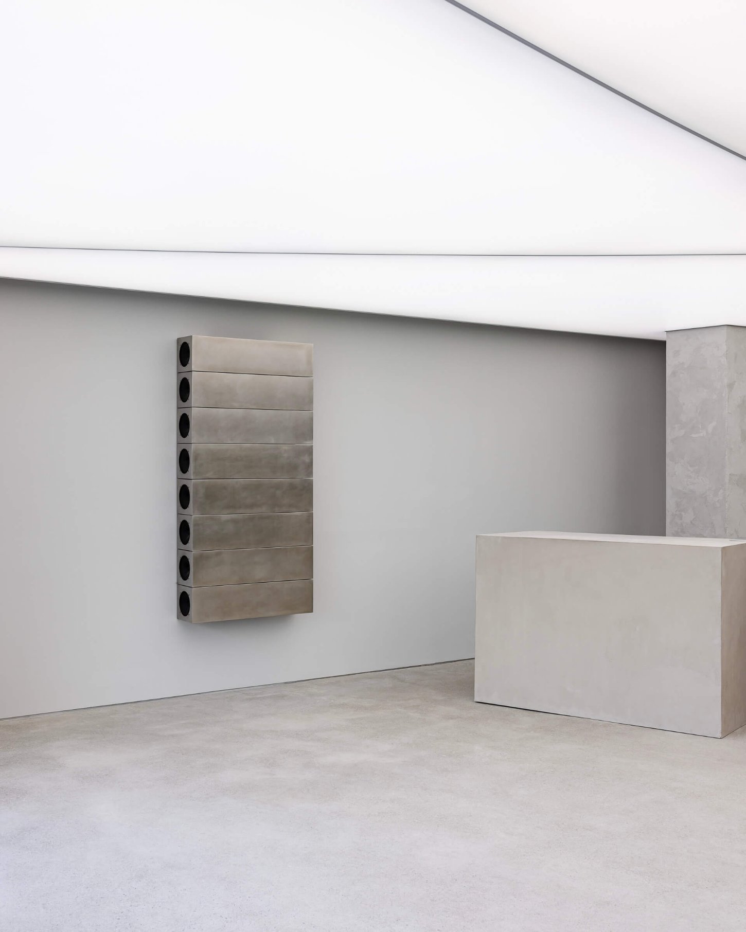 Mardi Mercredi store by Creative Studio Unravel — A minimalist retail interior featuring a wall-mounted horizontal metal storage unit with eight stacked compartments in brushed steel, each fitted with...