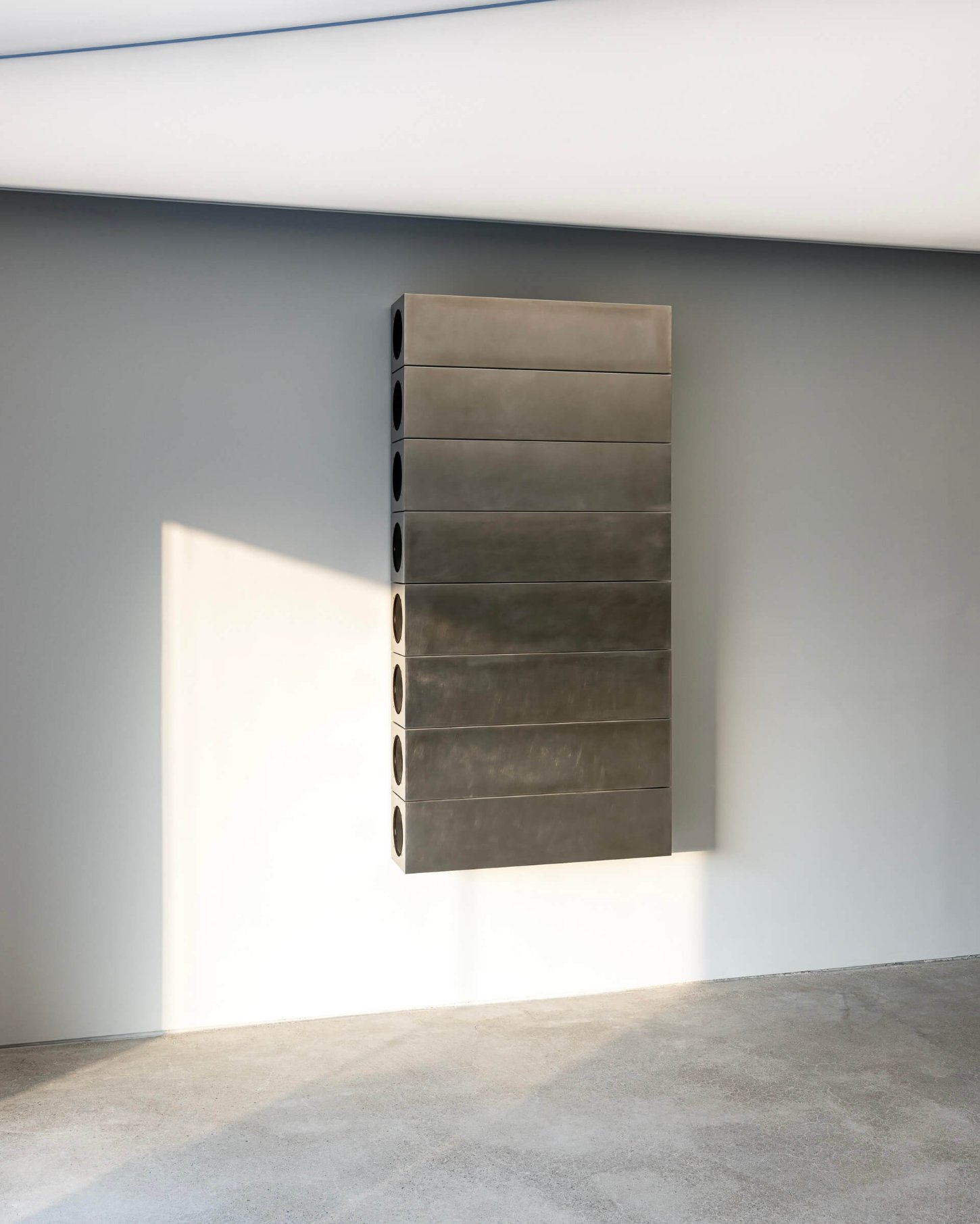 Mardi Mercredi store by Creative Studio Unravel — A wall-mounted steel storage unit dominates the gallery space, its eight horizontal compartments stacked vertically with circular ventilation ports punched...