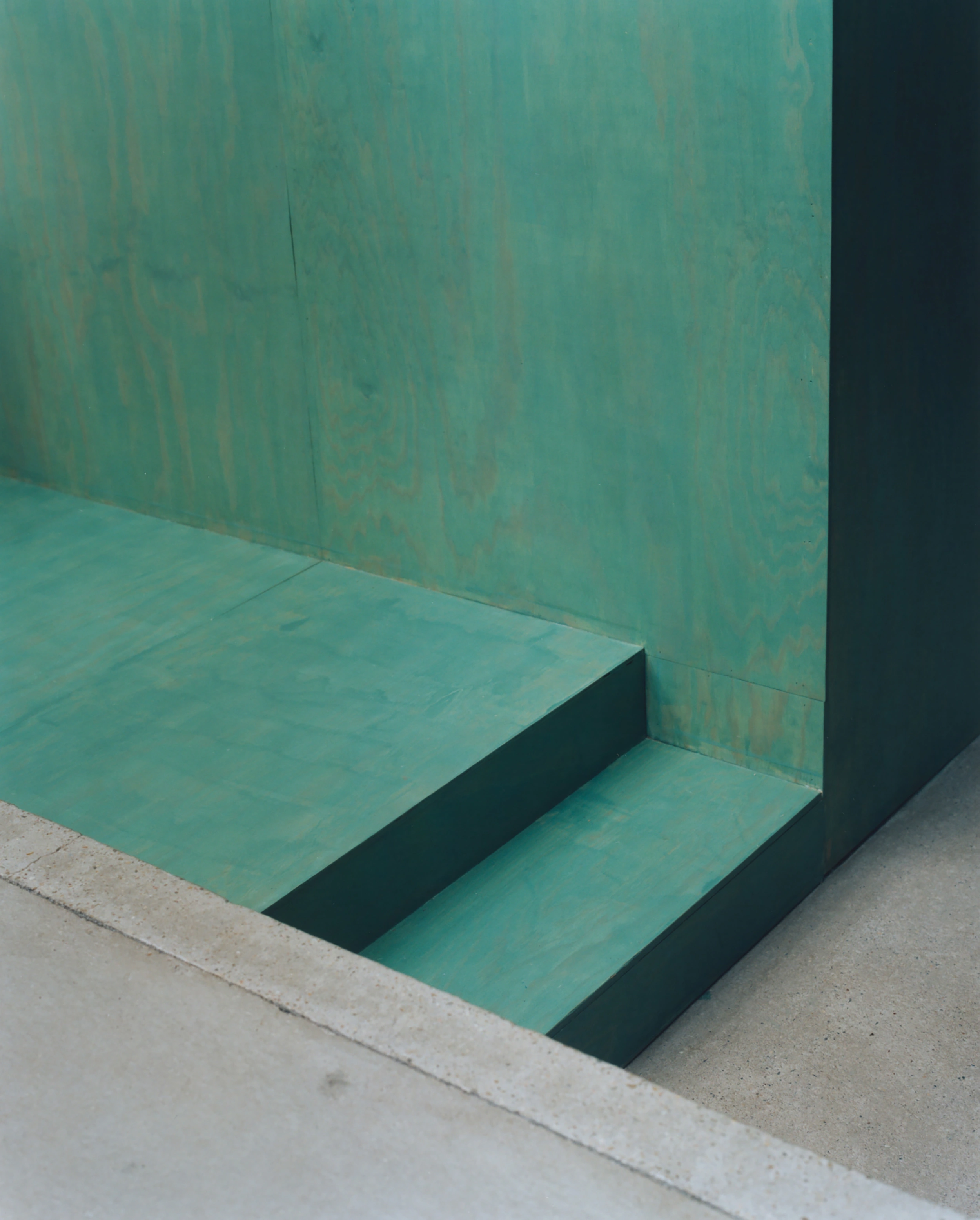 Erika and Willi's Barn by Piertzovanis Toews — A stepped entrance detail in patinated copper-green metal, revealing the threshold between exterior concrete and interior space.