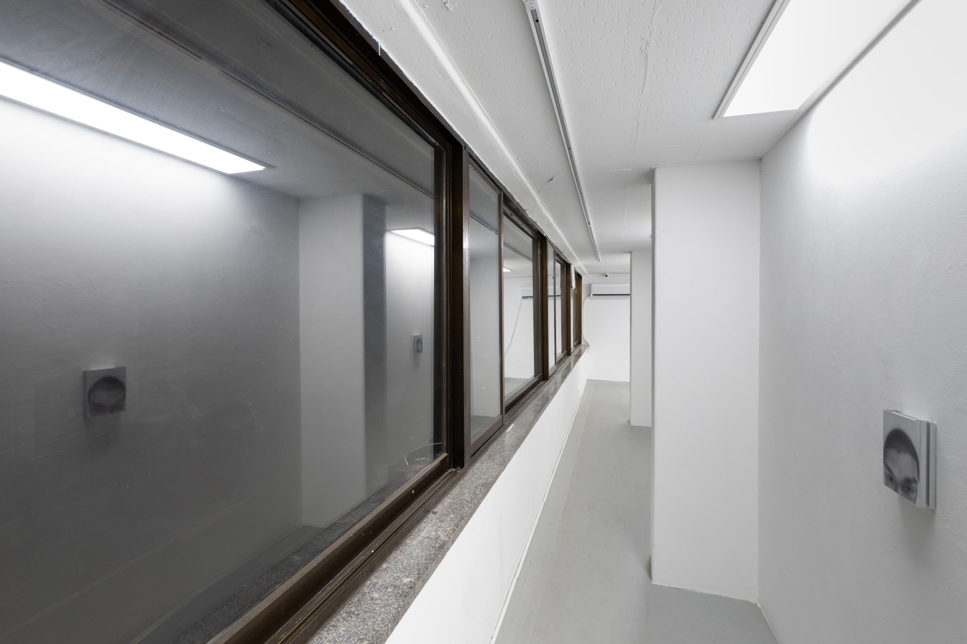 Offline Body by Myungchan Kim at dive.seoul — A narrow gallery corridor lined with translucent panels mounted along one wall, their charcoal-toned silhouettes visible against frosted glass.