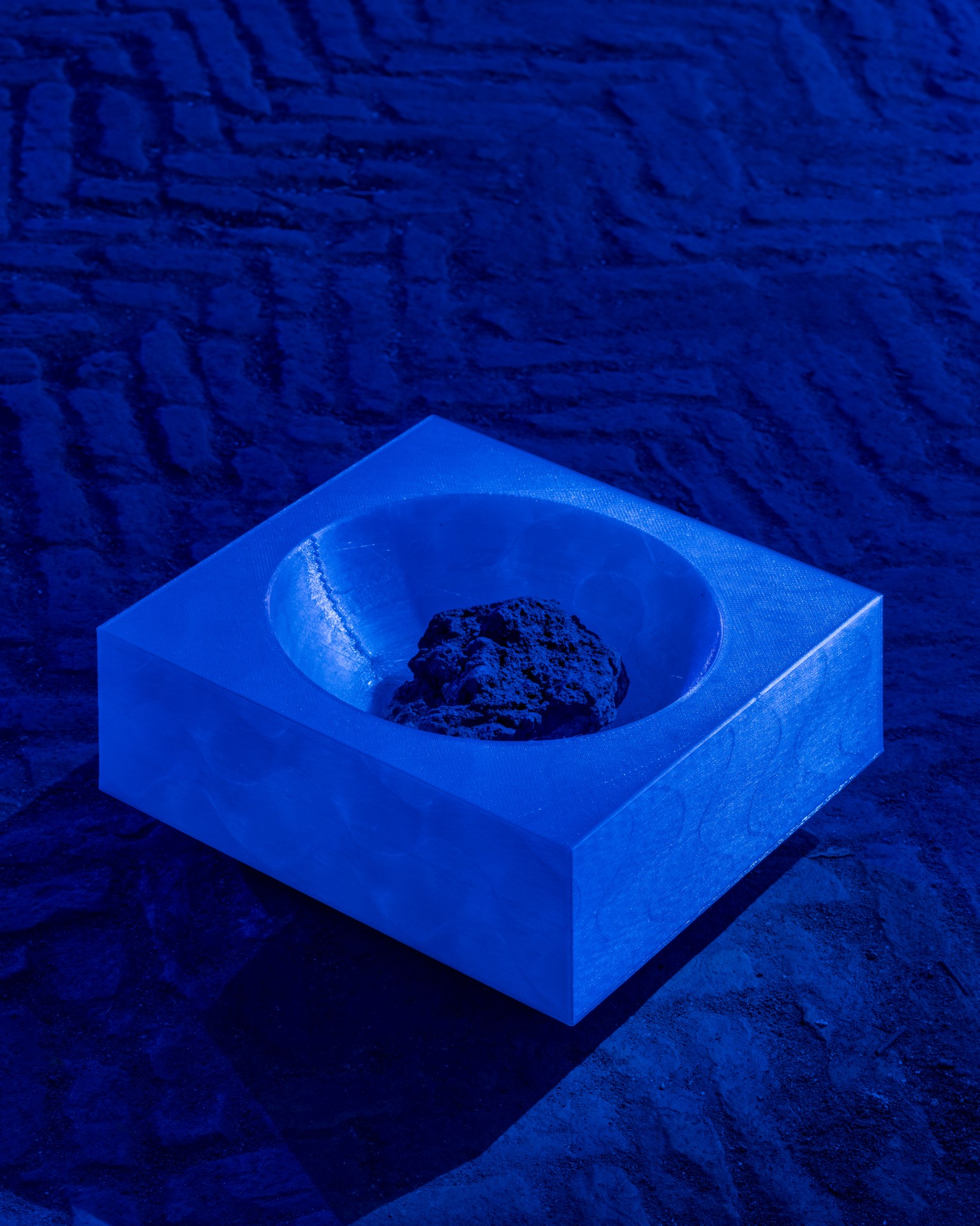 Techno Mythologies by Wang & Söderström at Christian IV’s Brewery — A bright blue resin or cast vessel sits centered on a textured blue-toned concrete floor, its interior cavity holding a dark, mineralized stone or...
