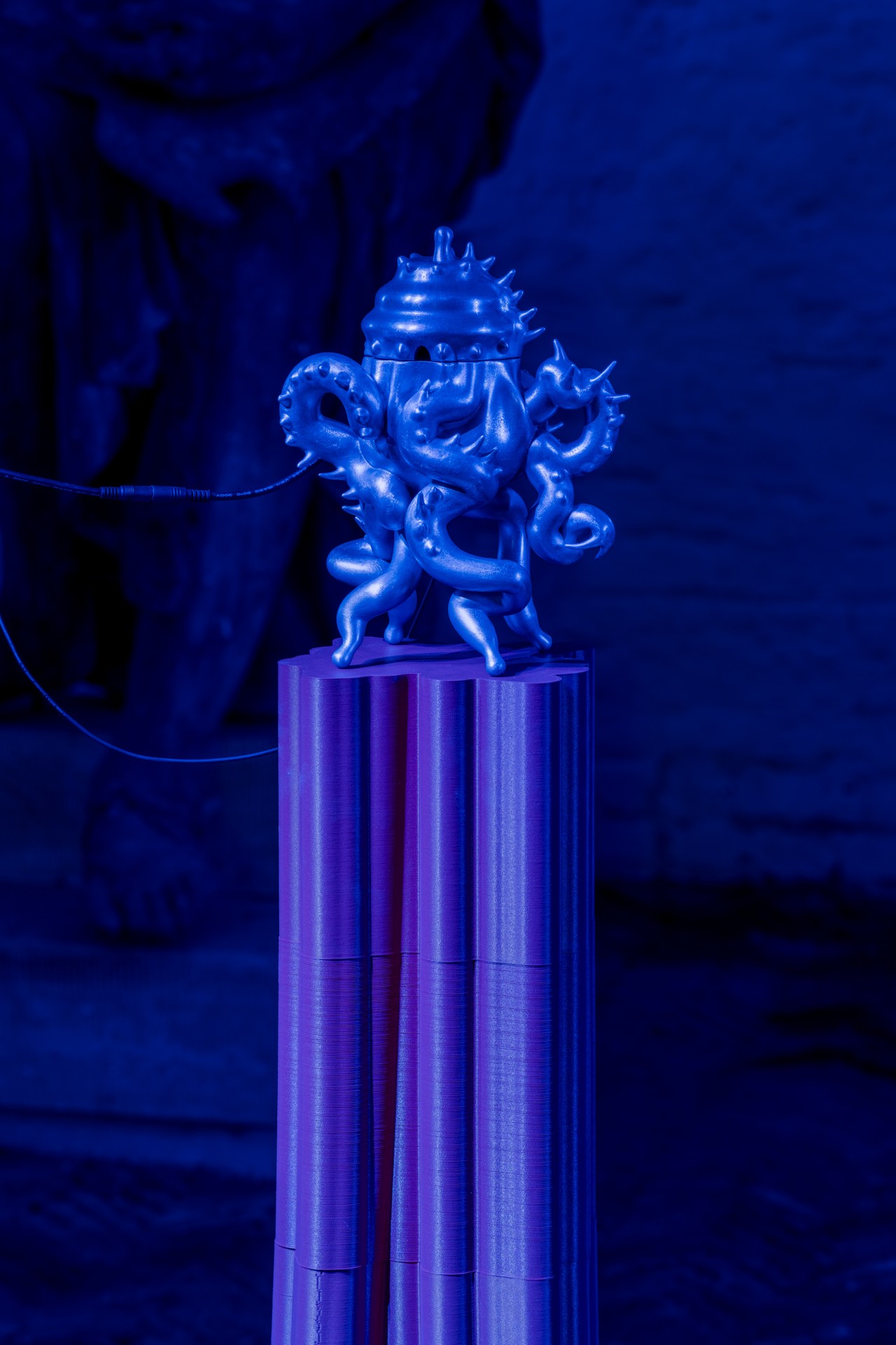 Techno Mythologies by Wang & Söderström at Christian IV’s Brewery — A sculptural installation mounted on a ribbed cylindrical plinth under saturated blue monochromatic lighting.