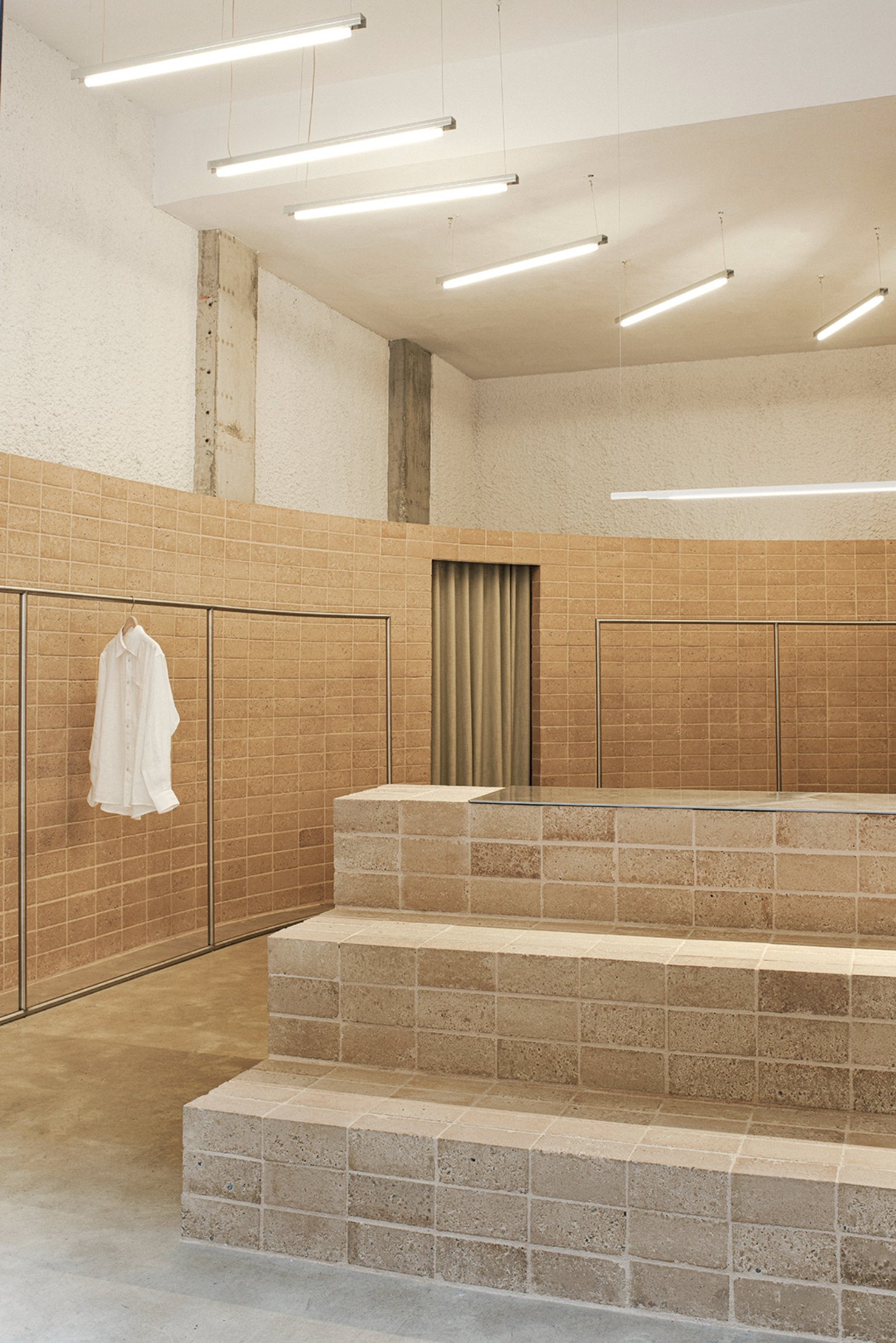 Neutrale by estudio DIIR — A showroom interior featuring a stepped retail display with travertine block construction rising from a polished concrete floor.