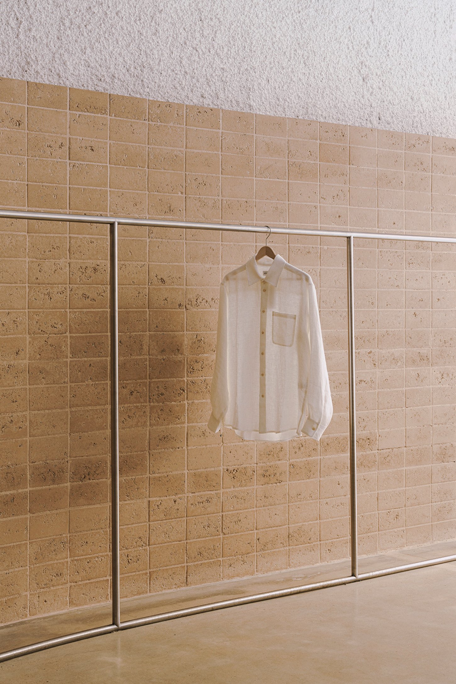 Neutrale by estudio DIIR — A cream-colored linen shirt hangs centered against a terracotta ceramic tile wall, its ribbed fabric catching soft light.