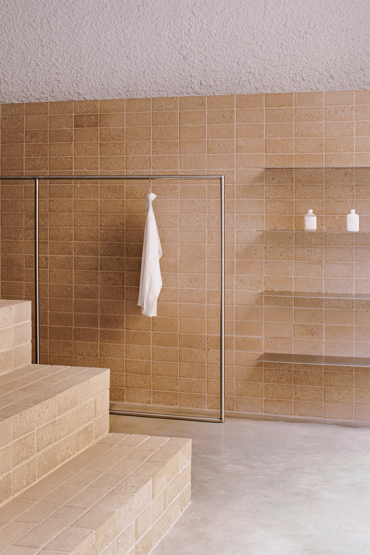 Neutrale by estudio DIIR — A terracotta tile wall with regular grid pattern and metal trim frames a minimalist retail display within Neutrale.