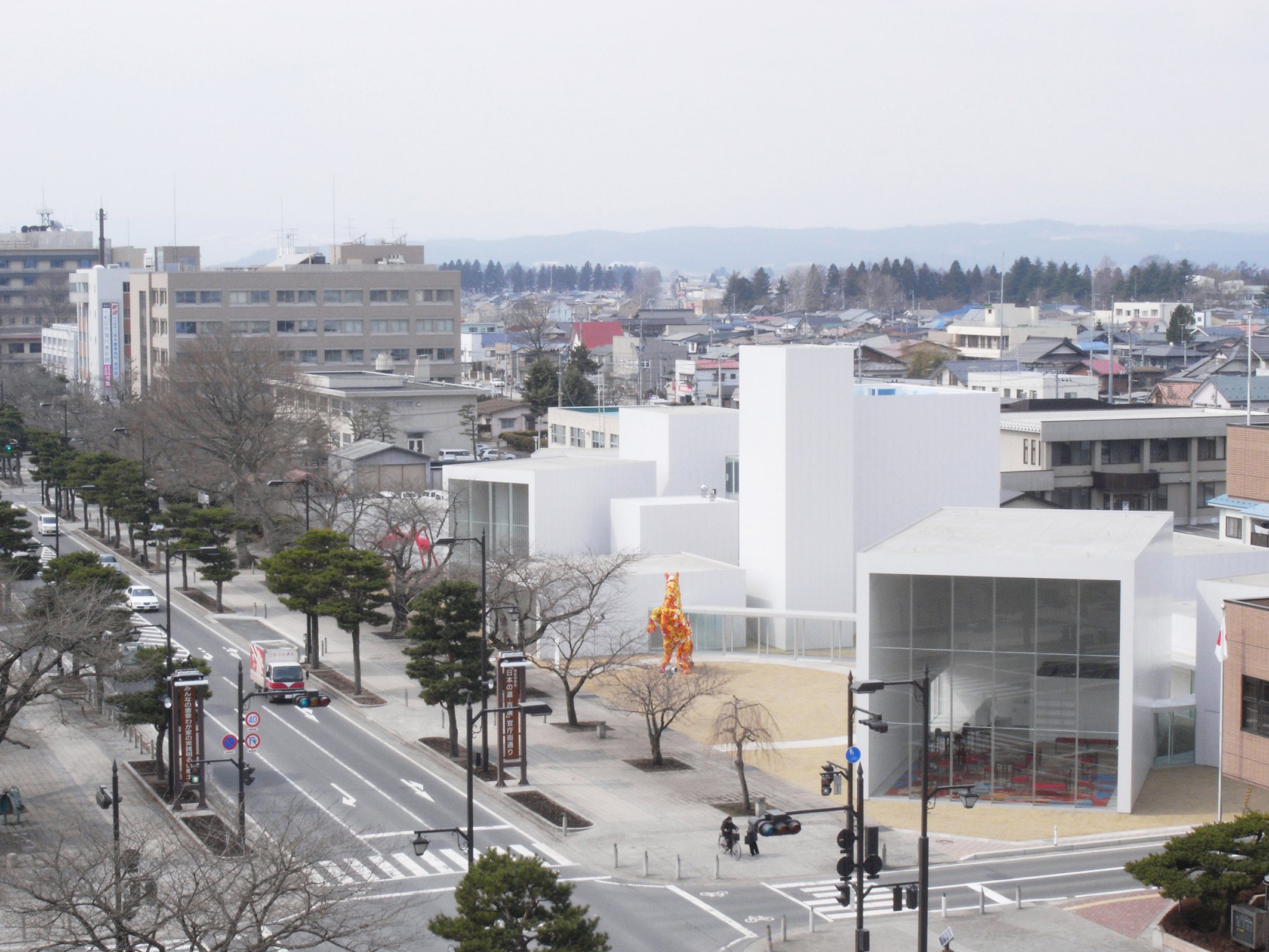 Towada Art Center by SANAA — Aerial perspective of Towada Art Center revealing the stepped white rendered volumes descending toward a landscaped plaza.