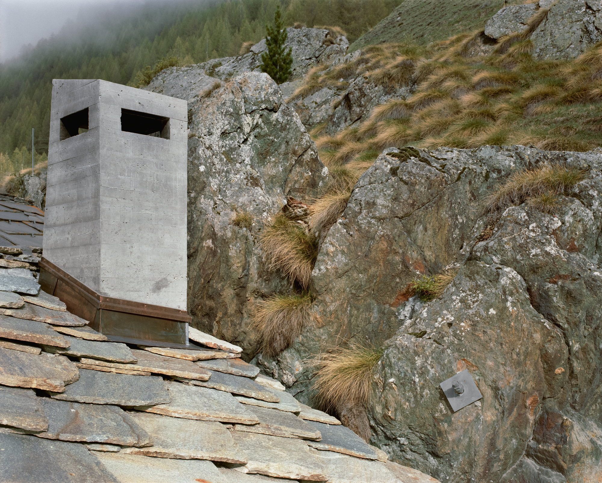 Lù Chatarme Transformation by Deschenaux Follonier by Deschenaux Architectes — A monolithic concrete structure with two horizontal apertures sits embedded against stratified alpine rock face.
