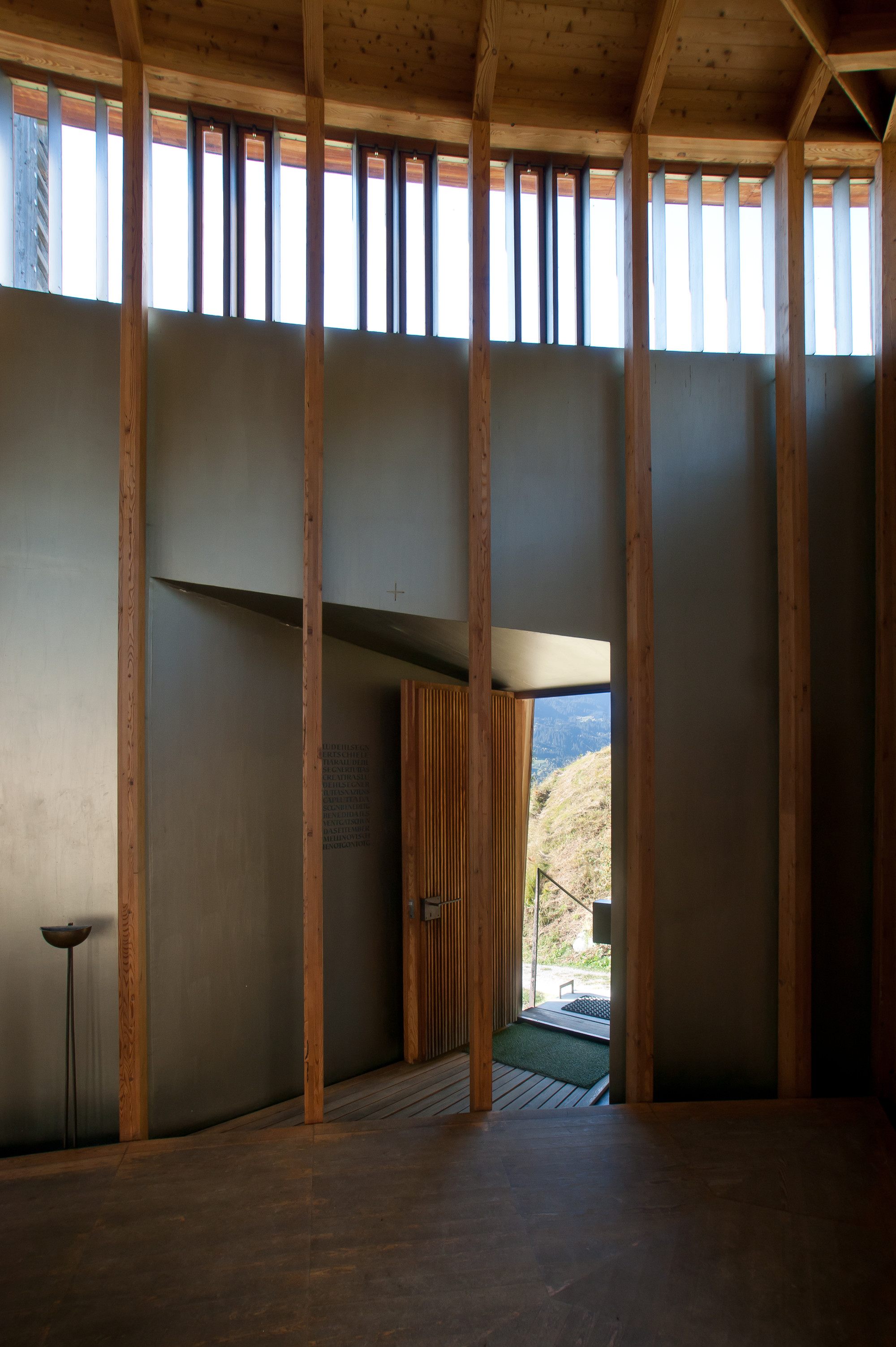 Saint Benedict Chapel by Peter Zumthor — Interior view of the chapel showing the post-and-beam timber frame structure with vertical wooden columns supporting the wooden ceiling.