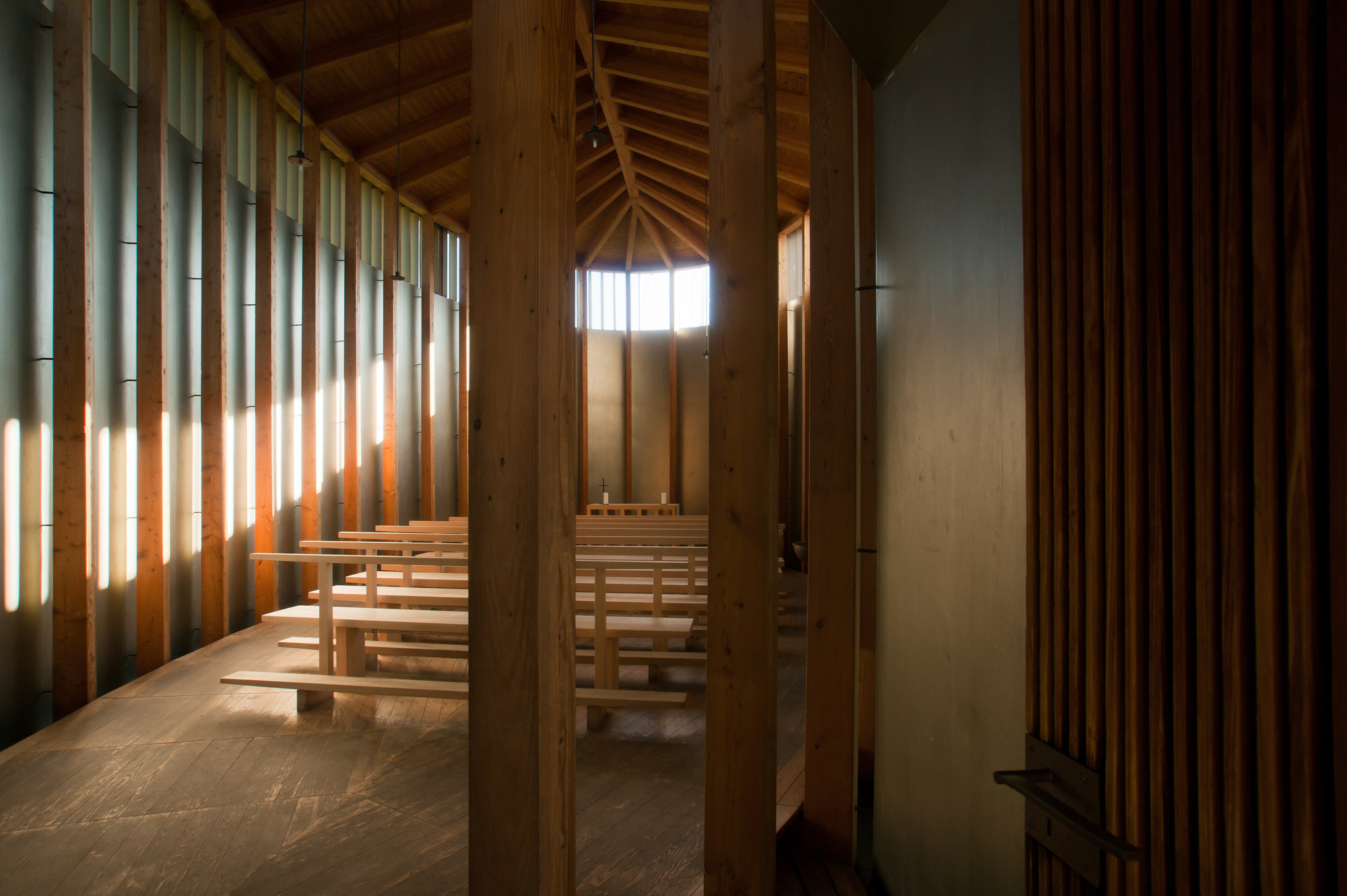 Saint Benedict Chapel by Peter Zumthor — The chapel's interior reveals a post-and-beam timber structure with substantial wooden columns supporting an exposed pitched-roof frame.