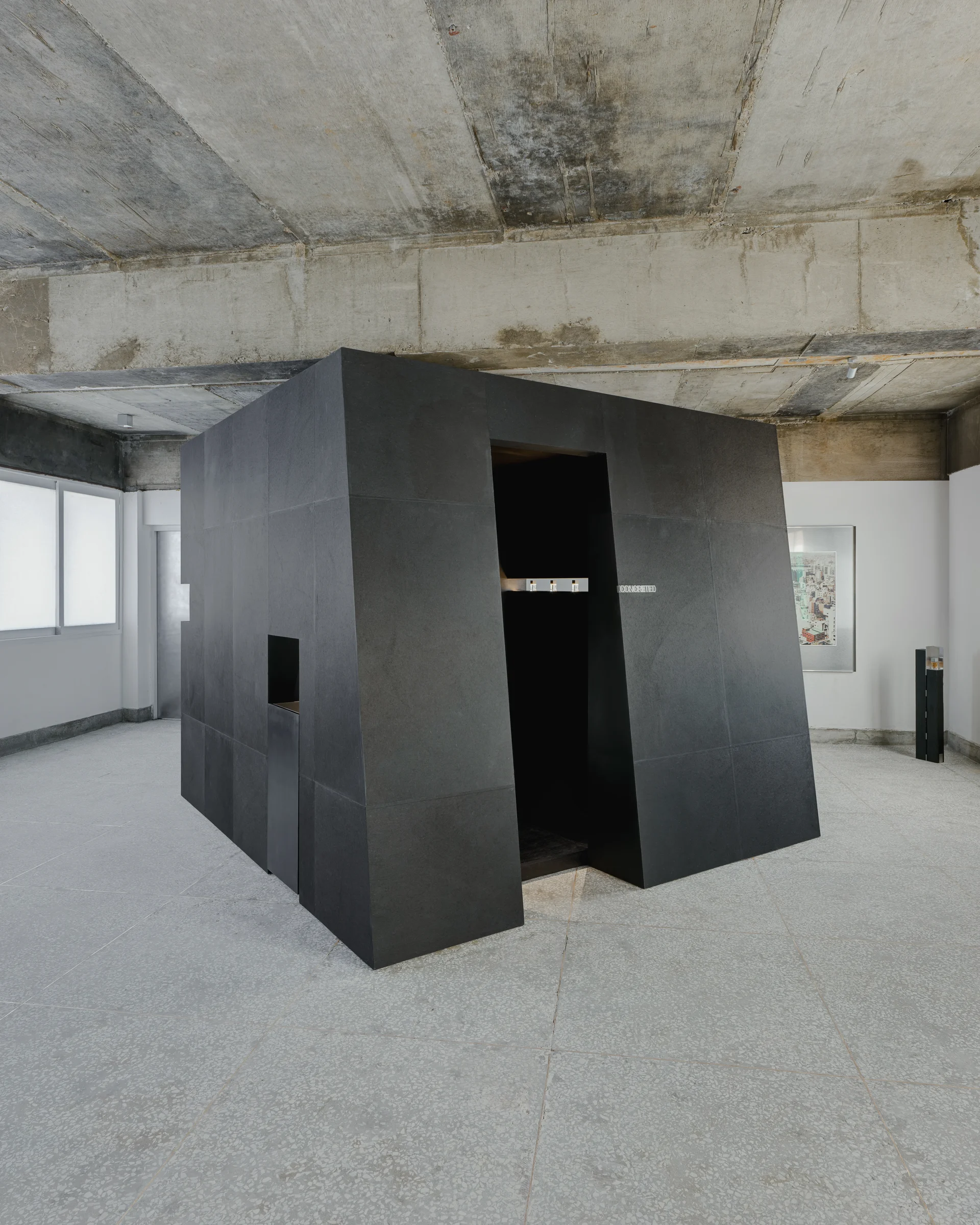 CONCRETED by molae, photographed by Noh Pu Reum — A monolithic black structure occupies the corner of a concrete-paneled interior, functioning as a display unit for the CONCRETED fragrance showroom.