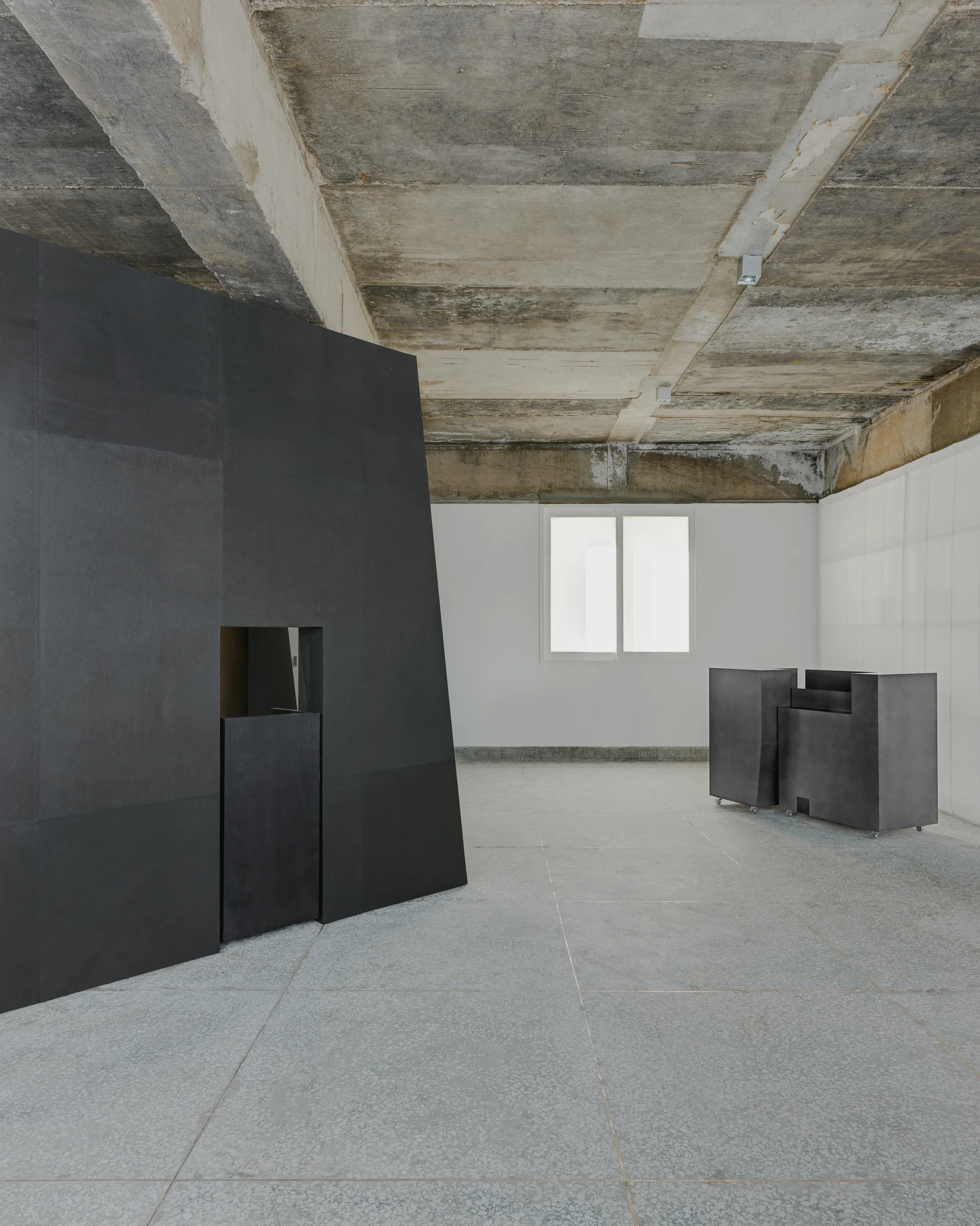 CONCRETED by molae, photographed by Noh Pu Reum — A monolithic black structure occupies the center of a raw concrete interior, its angular form cutting through the brutalist showroom space.