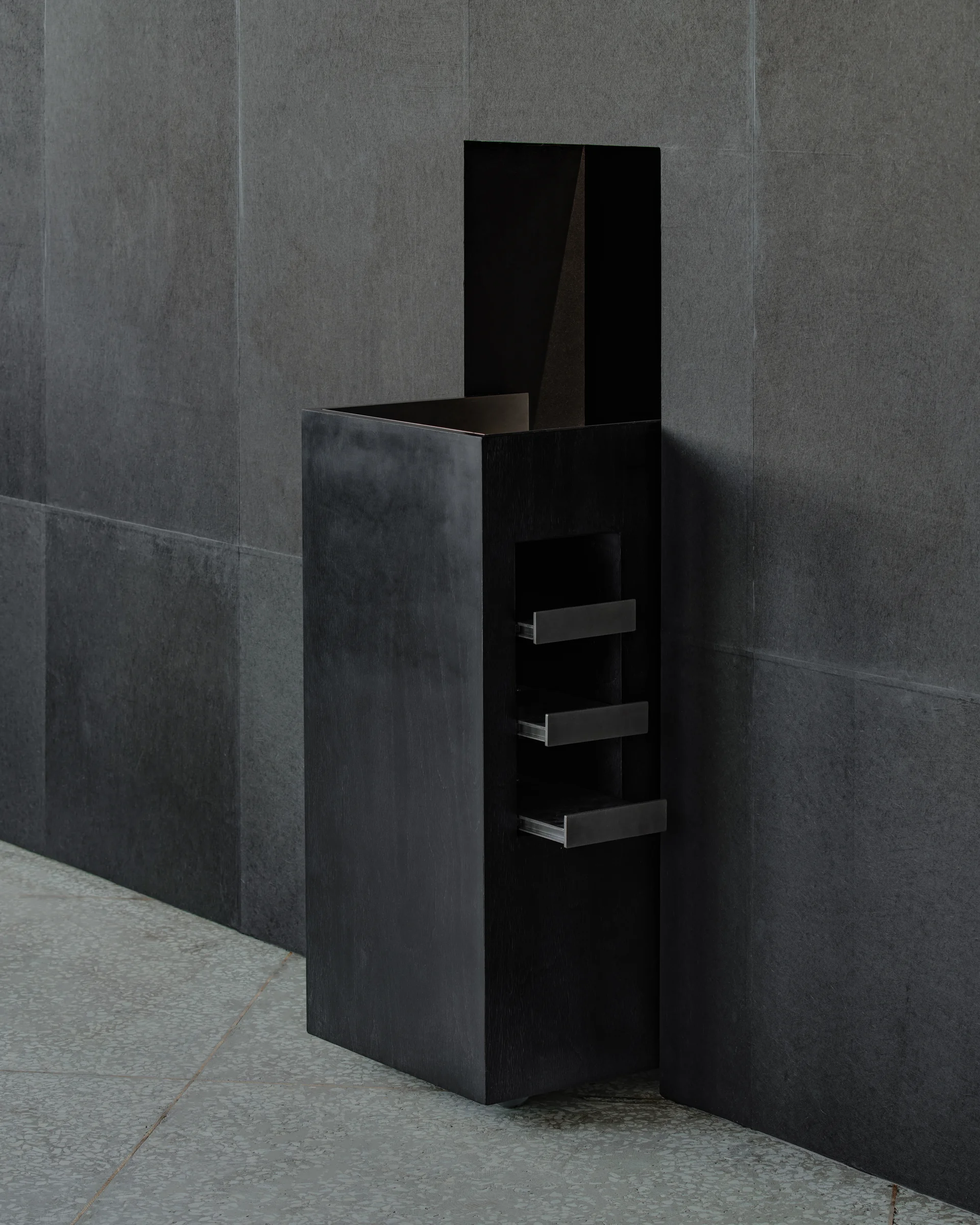 CONCRETED by molae, photographed by Noh Pu Reum — A mobile display unit occupies a corner of the Seoul showroom, its composition anchored by vertical black steel planes that frame a modular grid of light grey panels.