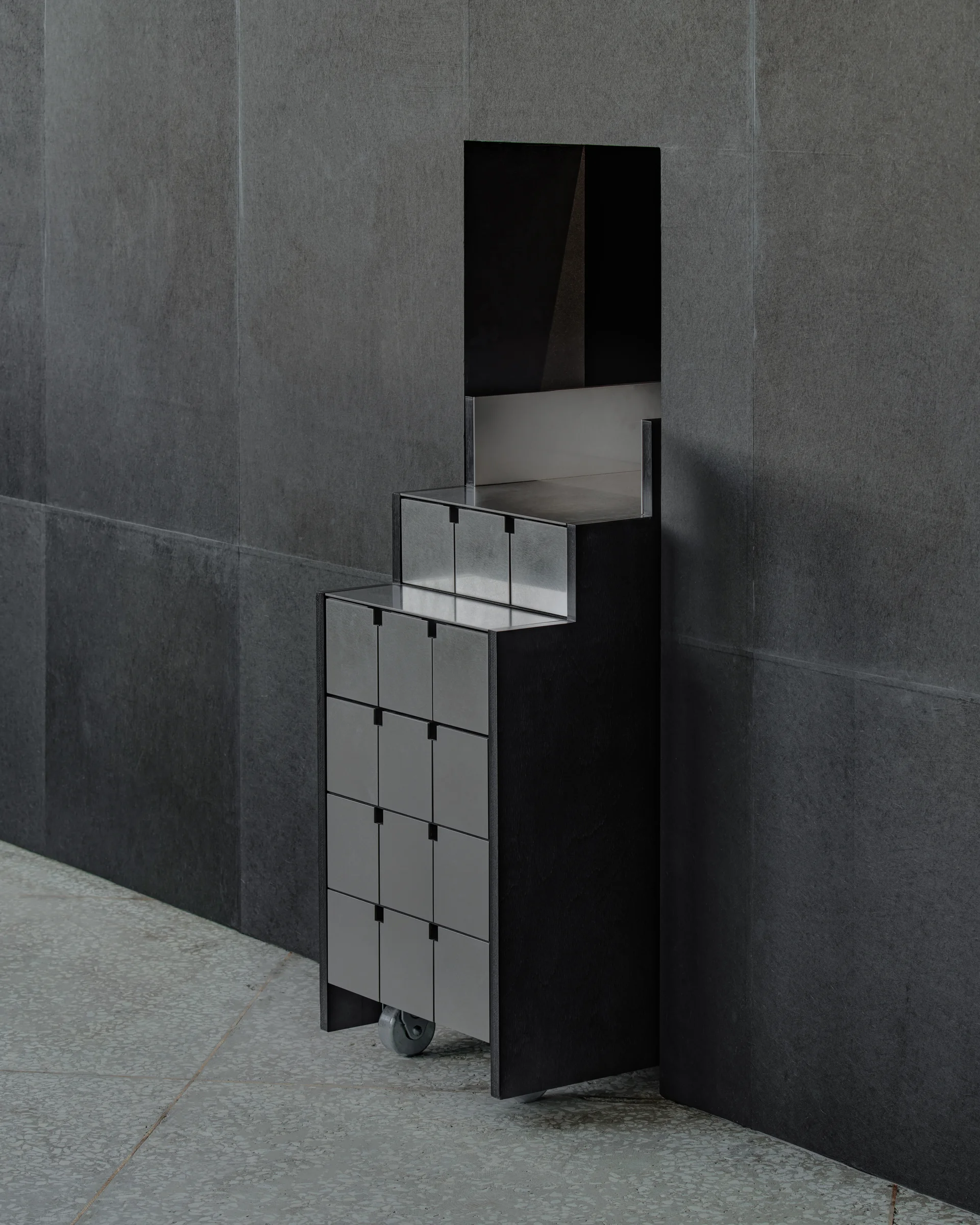 CONCRETED by molae, photographed by Noh Pu Reum — A tall, narrow wooden display structure occupies a corner of the Seoul showroom, its charcoal-stained timber surface punctuated by a vertical slot running the full height.