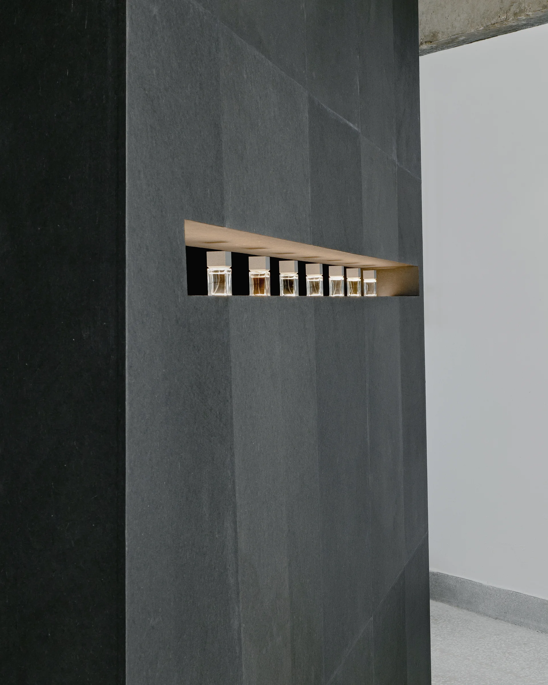 CONCRETED by molae, photographed by Noh Pu Reum — A tall, monolithic black display tower stands centered in the showroom, its tapered trapezoidal form rising against translucent white curtain panels.