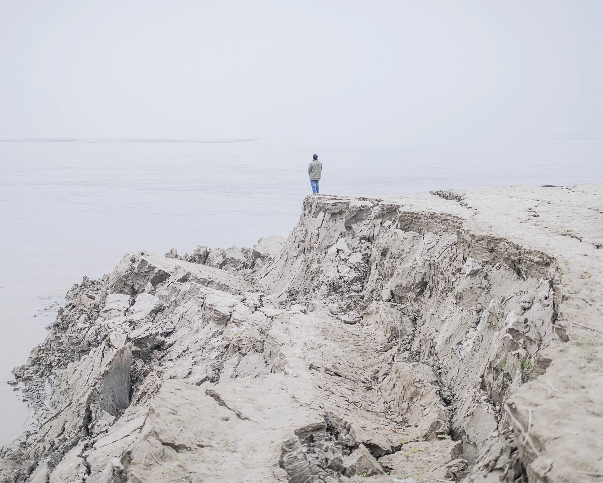 Leen / Jirno / Awngar by Sarker Protick, photographed by Sarker Protick — A figure with long grey hair, photographed from behind, wears a cream-colored cotton garment printed with red and burgundy floral patterns.
