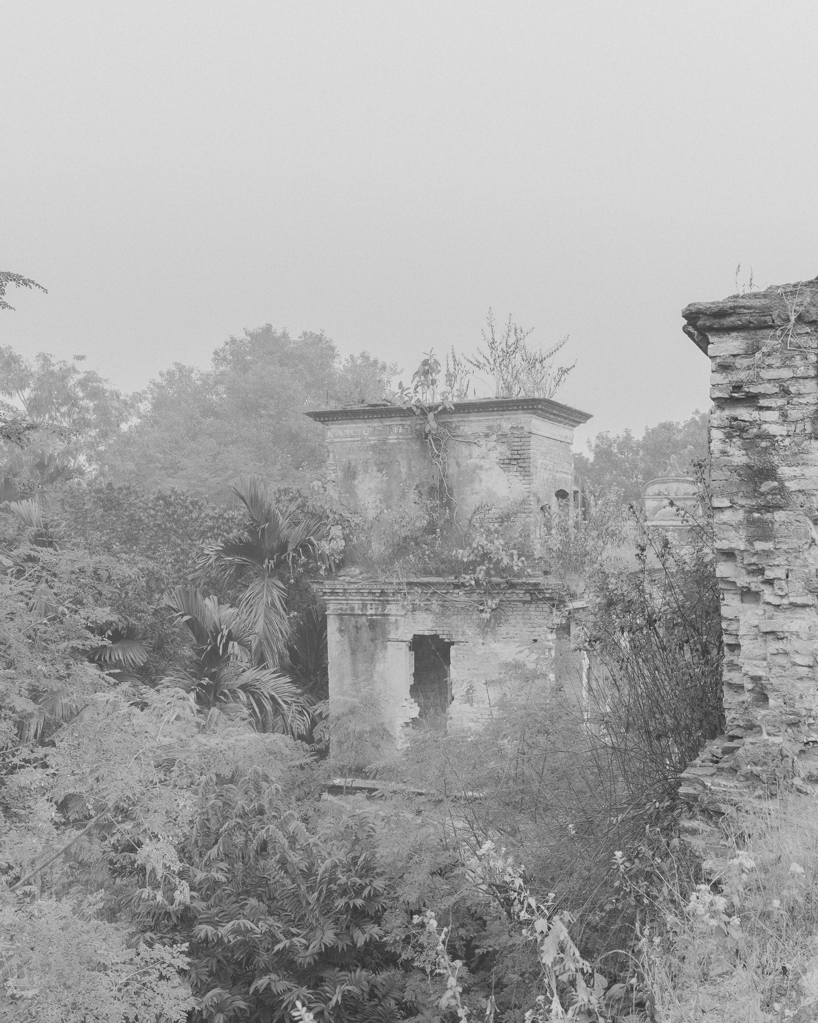 Leen / Jirno / Awngar by Sarker Protick, photographed by Sarker Protick — A solitary figure in blue stands fishing on a concrete platform beneath a massive bridge support, its cylindrical column rising vertically into mist.