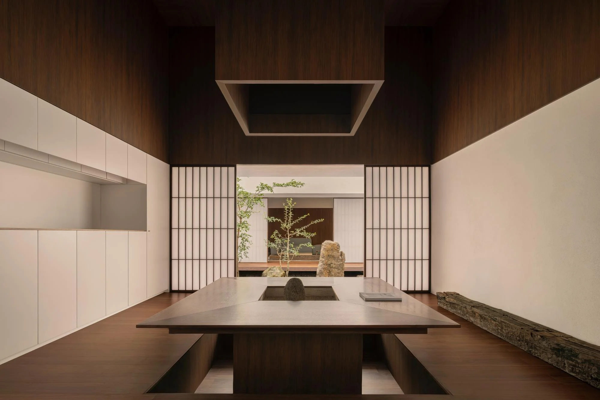 Kehai House by HW Studio, photographed by César Béjar, Gustavo Quiroz — A centered view through timber-framed sliding doors reveals a sunken courtyard anchored by sculptural stone elements and a young tree.