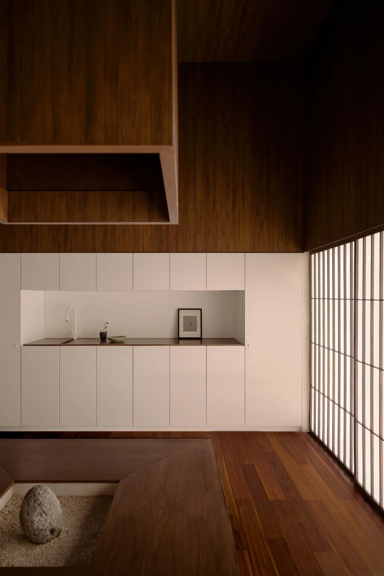 Kehai House by HW Studio, photographed by César Béjar, Gustavo Quiroz — The kitchen alcove features floor-to-ceiling cabinetry in soft cream or pale grey, organized as vertical stacked panels with integrated sink and minimal hardware.