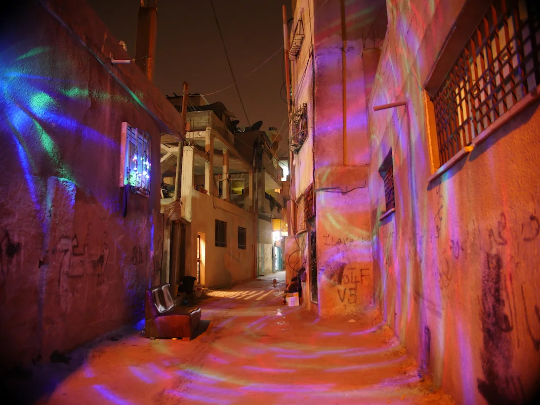Landing by Maen Hammad, photographed by Maen Hammad — A narrow alleyway in the West Bank is transformed by artificial colored lighting—predominantly magenta, purple, and orange hues cast across render and concrete walls.