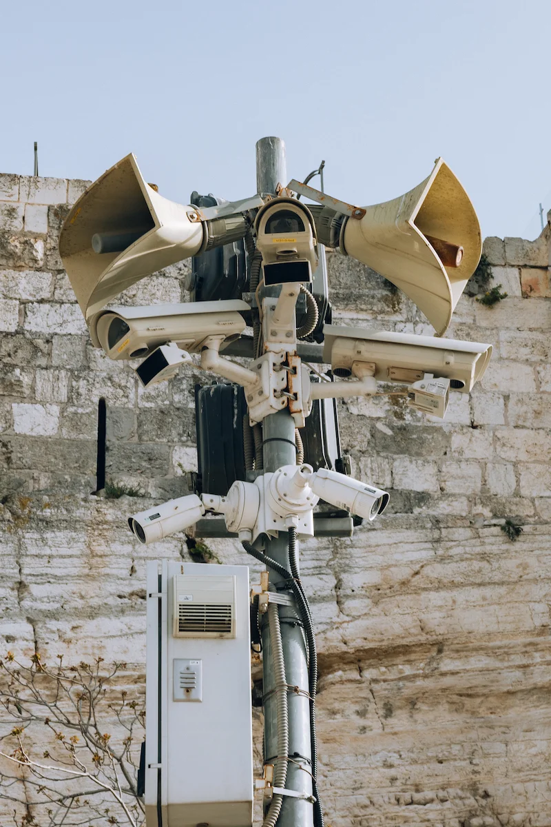 Landing by Maen Hammad, photographed by Maen Hammad — A figure carries labor tools and supplies across arid Palestinian terrain, their face obscured by a patterned headwrap and backpack.