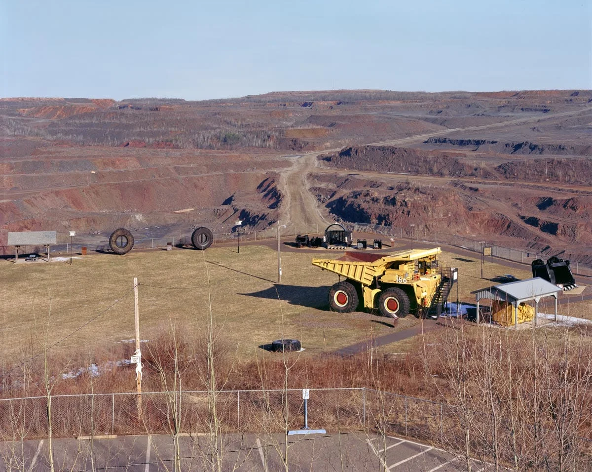 National Character by John Sanderson, photographed by John Sanderson — A bustling auto salvage yard in an urban industrial area, captured at ground level amid active commerce and repair work.