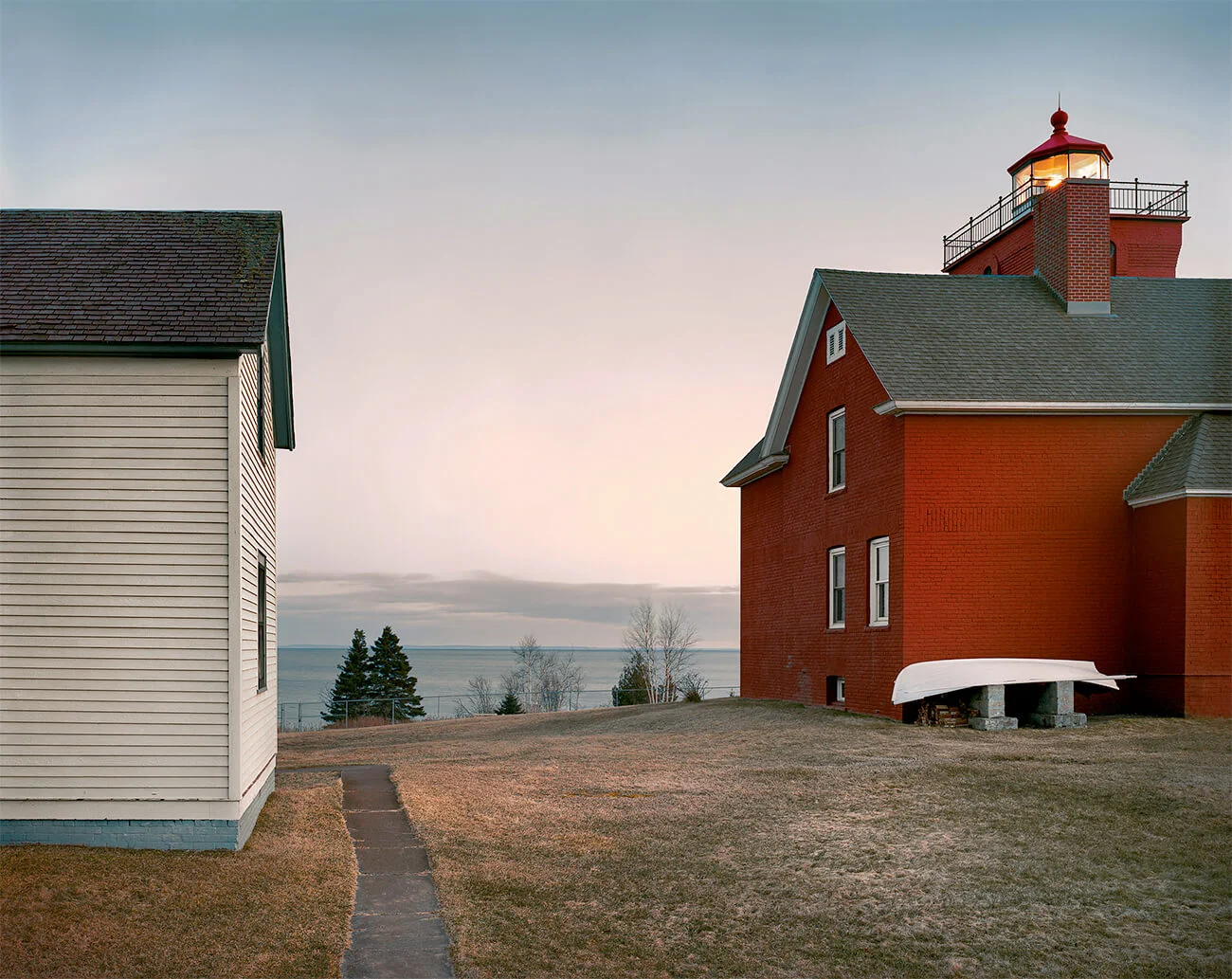National Character by John Sanderson, photographed by John Sanderson — A multi-generational family portrait staged on the front porch of a rural residence, positioned against white-painted wood siding and supporting columns.