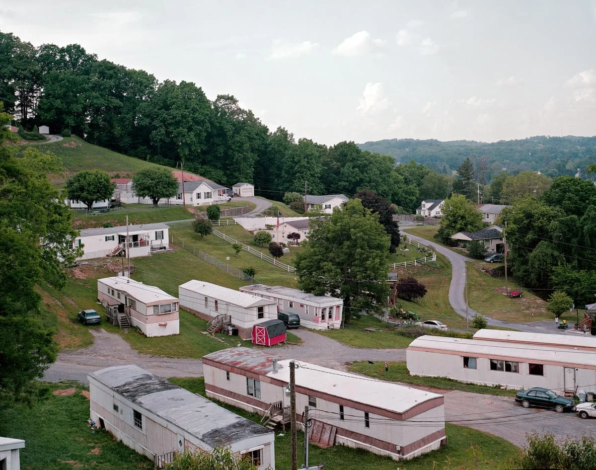 National Character by John Sanderson, photographed by John Sanderson — A deteriorating industrial complex dominated by a massive black steel-frame structure with gridded fenestration, its expanse marked by faded painted signage reading 'SYNDROMANIA' and '