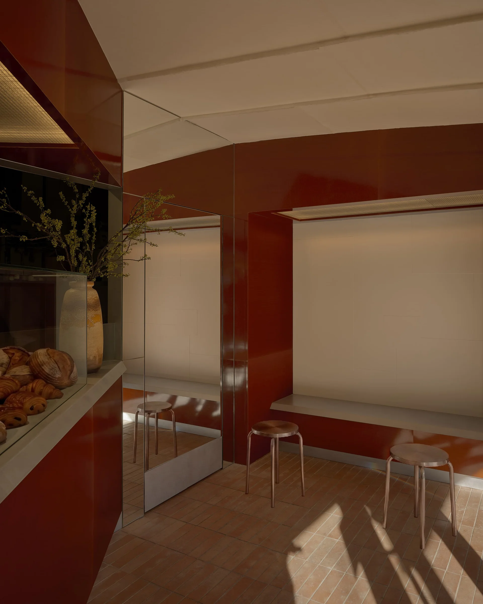 Diljān Afghan Bakery by New Body, photographed by Sean Davidson — A display case set into a burgundy wall features a potted arrangement of anemone flowers with dark centers and pale petals, their stems arranged in a decorative vessel with red and gold pat