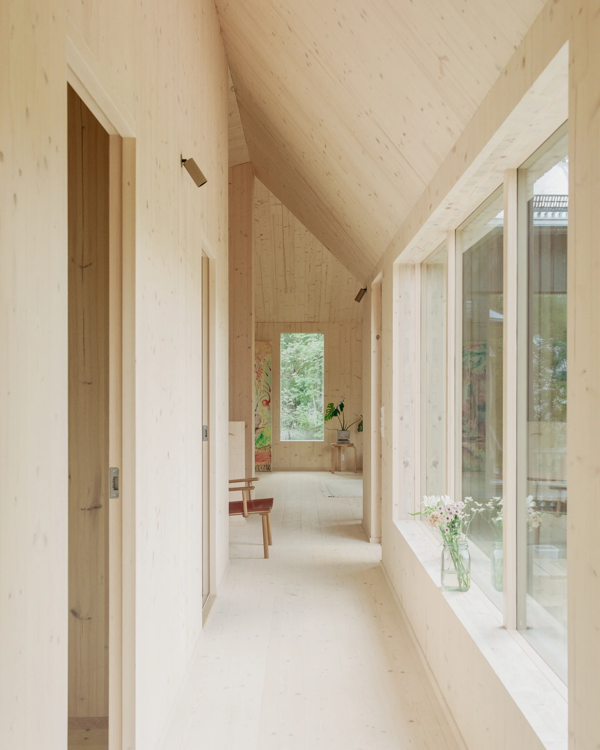 Villa Margo by Talli Ark, photographed by Kalle Kouhia — A covered timber deck extends from the dark-green exterior wall, framing a view into dense woodland.