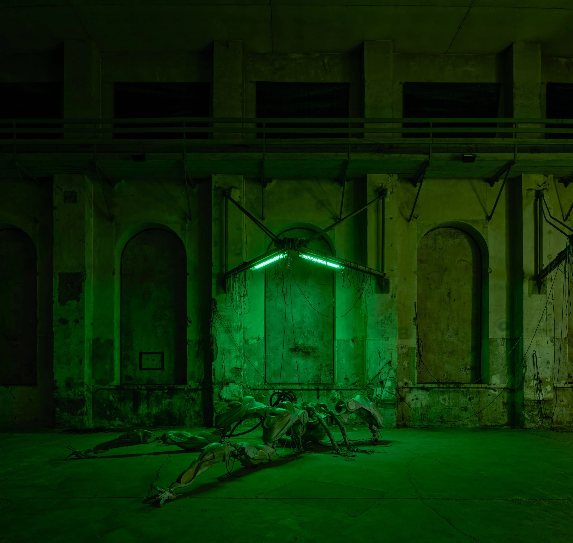 47°24’35’’N / 9°44’20’’E by Davide Allieri, photographed by Günter Richard Wett — Mecha (protective suit), 2026: the full creature viewed against three arched openings, a V-shaped neon fixture burning above it like a shrine lamp over a fallen pilot.