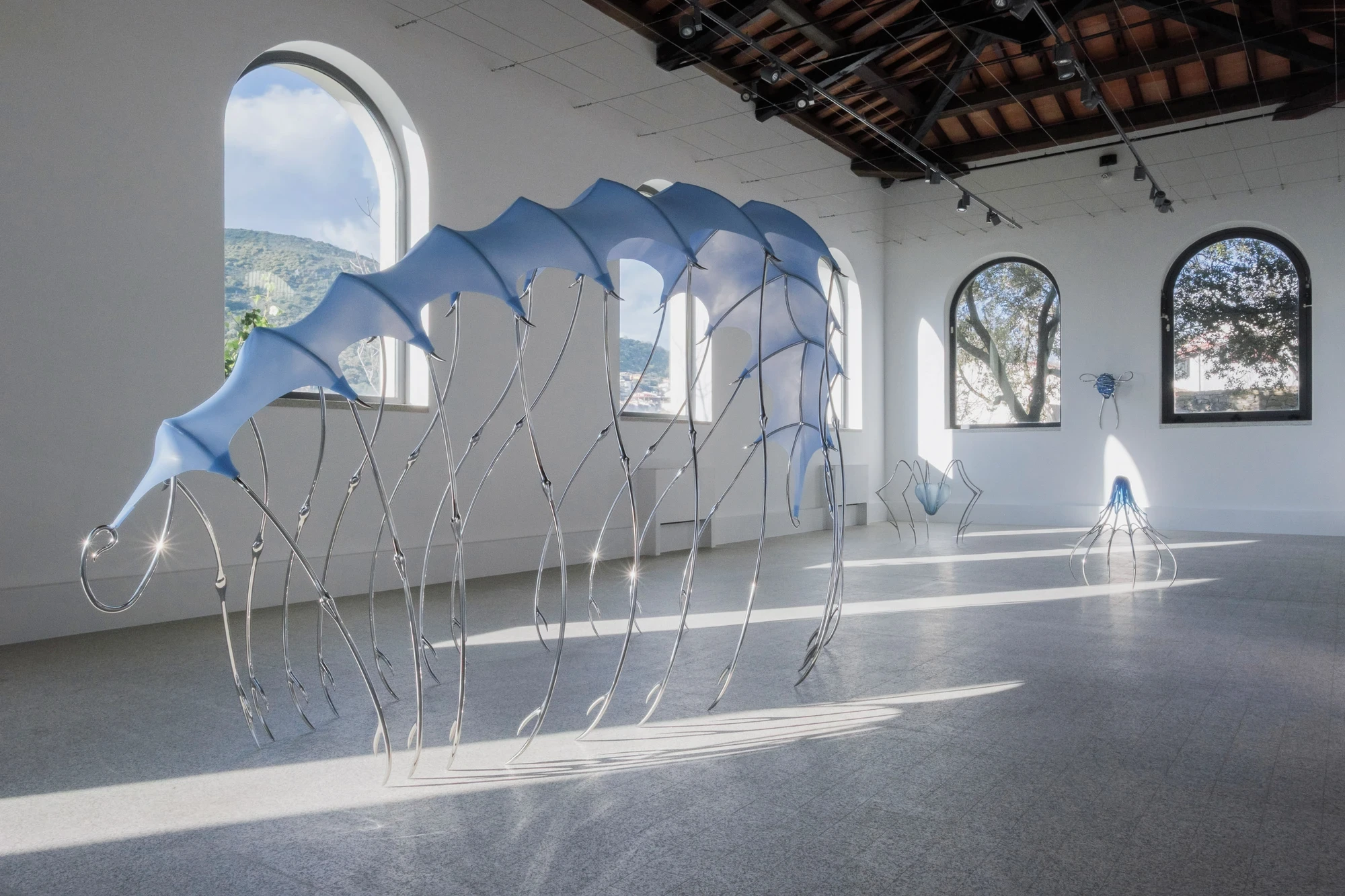 Blue Blooded — Sangue blu by Hannah Levy, photographed by Andrea Mignogna — wide view of the canopy along the nave, late sun raking across the terrazzo and through the silicone membrane to cast long shadows of the steel legs.
