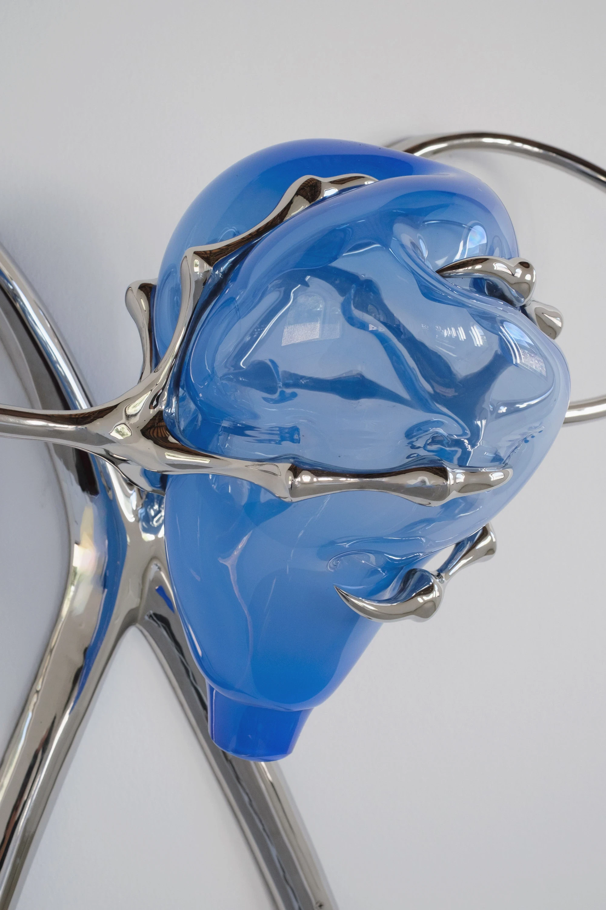 Blue Blooded — Sangue blu by Hannah Levy, photographed by Andrea Mignogna — close detail of polished steel claws compressing a bulb of blown blue glass, the glass deformed at the points of contact like skin under a tool.