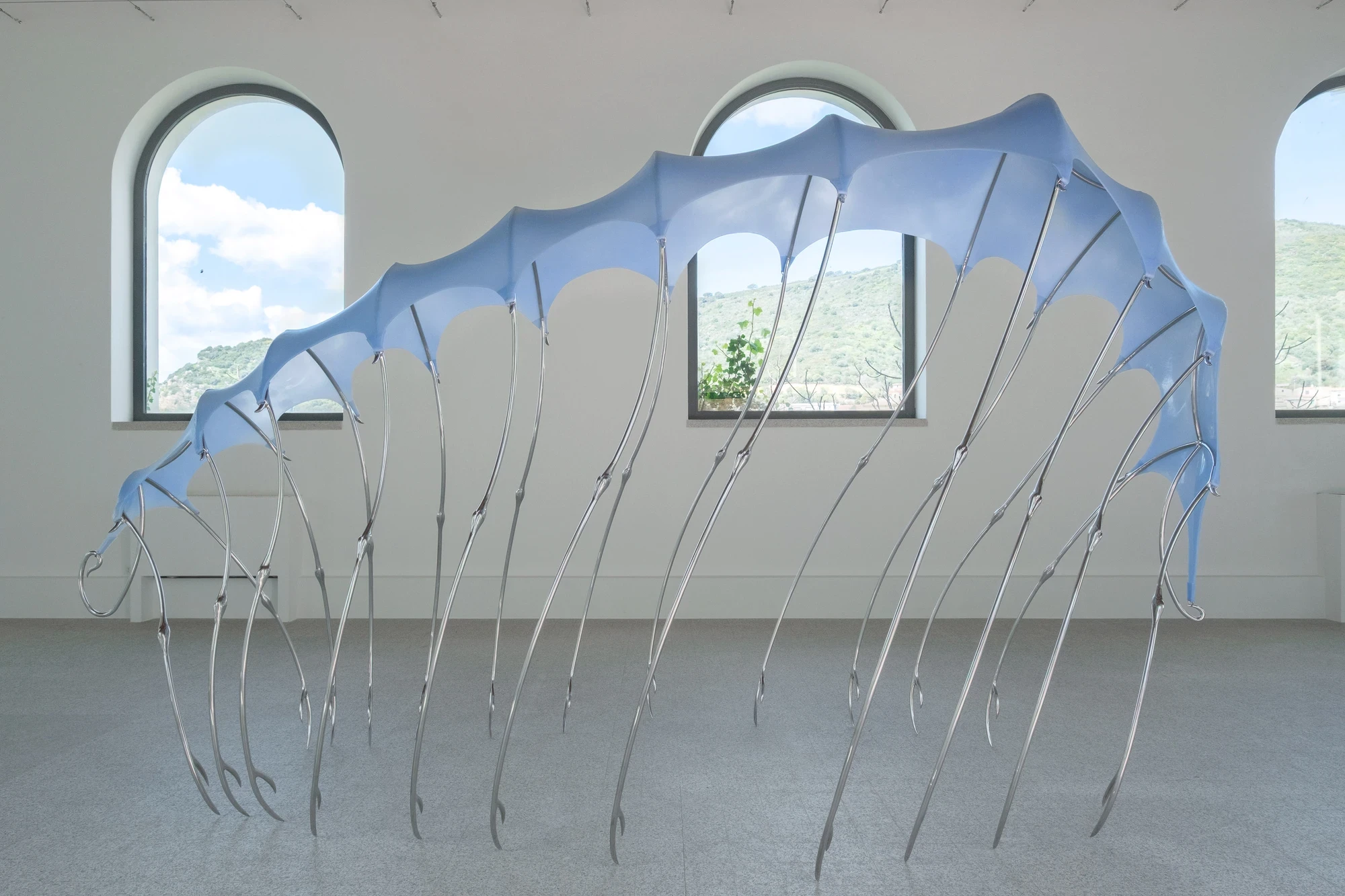 Blue Blooded — Sangue blu by Hannah Levy, photographed by Andrea Mignogna — the canopy seen in side elevation, stretched along the length of the washhouse nave with Sardinian hills visible through arched windows behind.