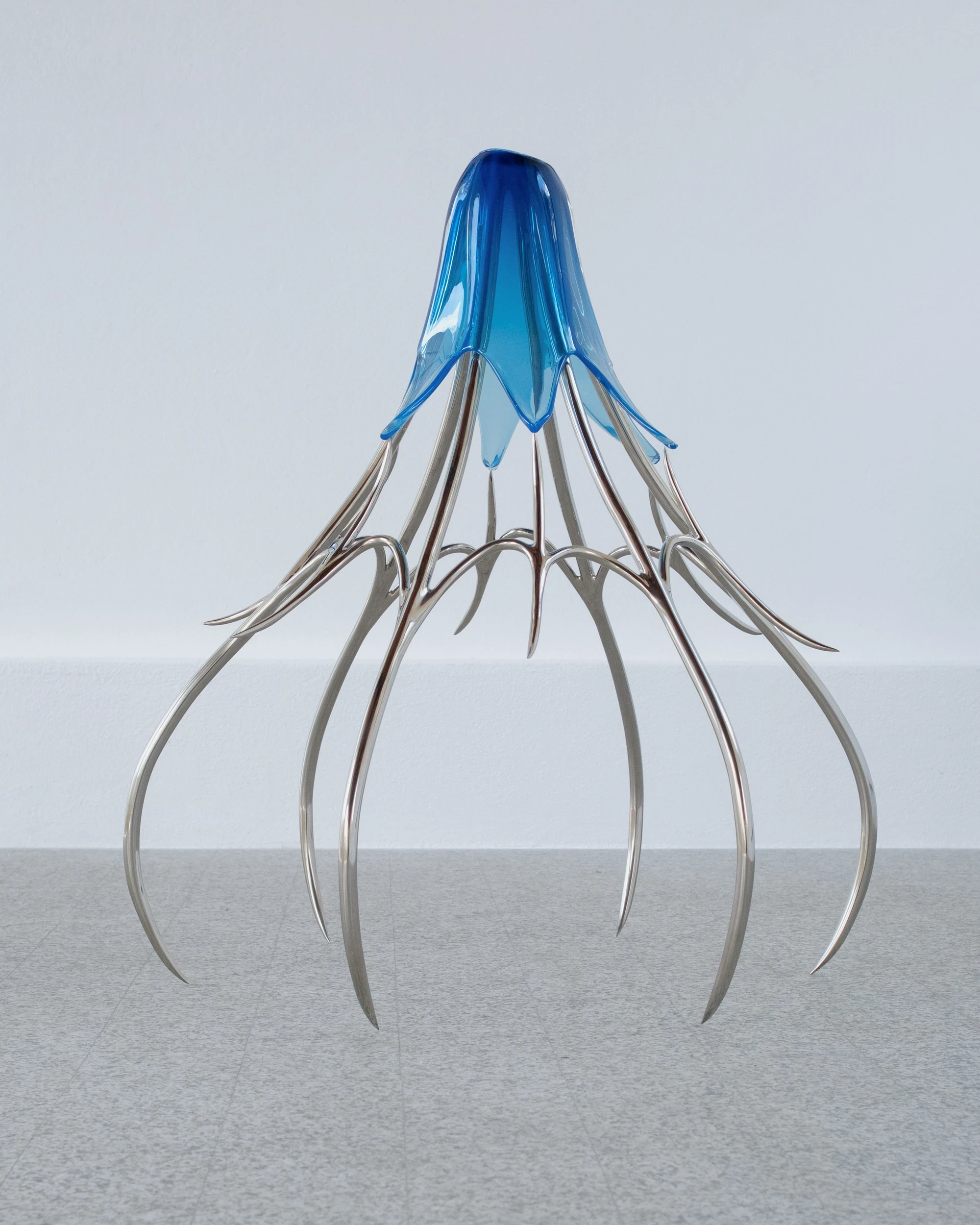 Blue Blooded — Sangue blu by Hannah Levy, photographed by Andrea Mignogna — isolated sculptural study of a blown blue-glass form perched on eight splayed steel legs that taper into claw tips on the terrazzo.