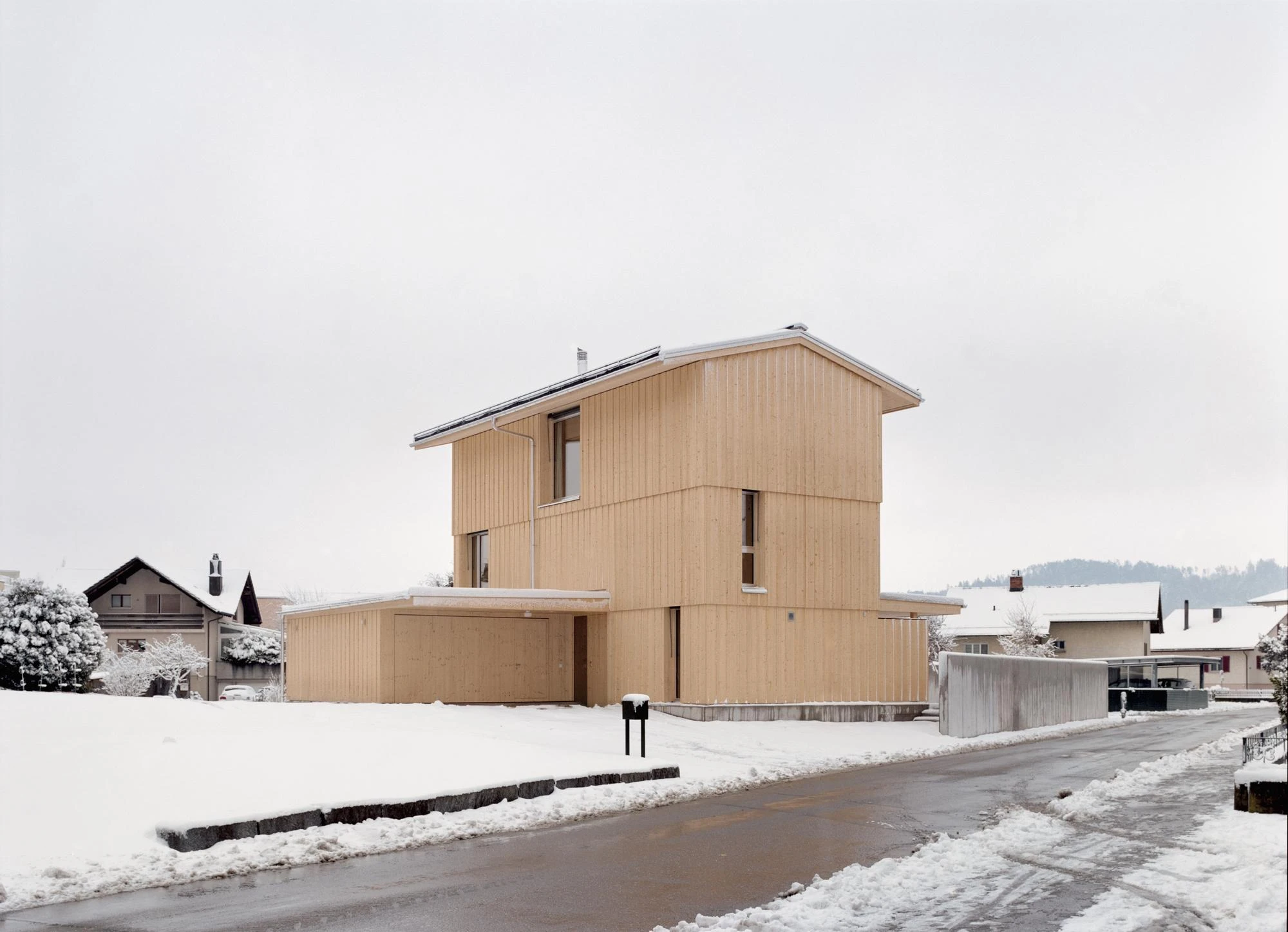 Tower House by kit, photographed by Till Forrer — Interior staircase hall: exposed concrete stair treads with galvanised steel balustrade uprights, spruce panels on the ceiling above, warm wall light.