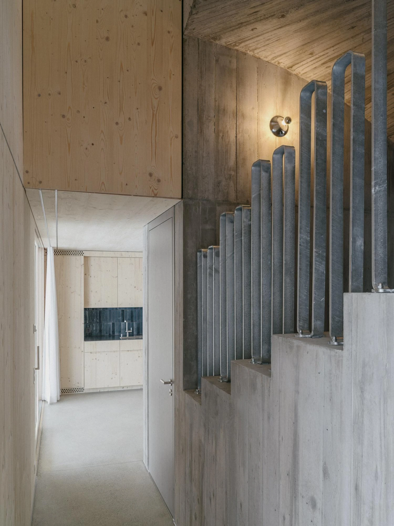 Tower House by kit, photographed by Till Forrer — Bedroom interior: white linen on the bed, spruce wall behind, a narrow vertical window cutting a slot of winter light through the facade.