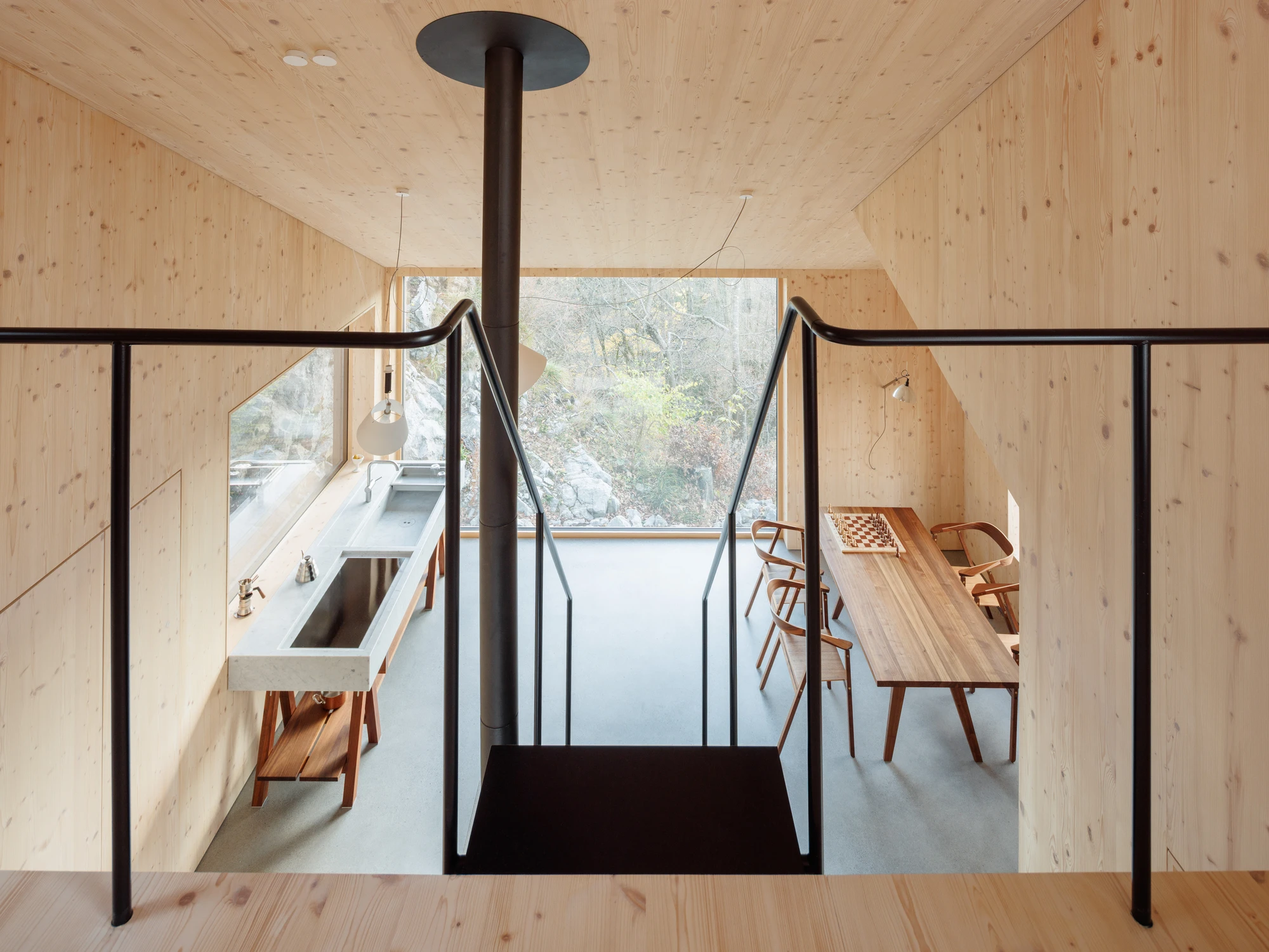 Swiss Alpine Cabin Reconstruction by Guča arch., photographed by Matej Hakár — Interior of the CLT-lined sauna: wood on all surfaces, a small bench, the stove in the corner, a narrow window toward the slope.