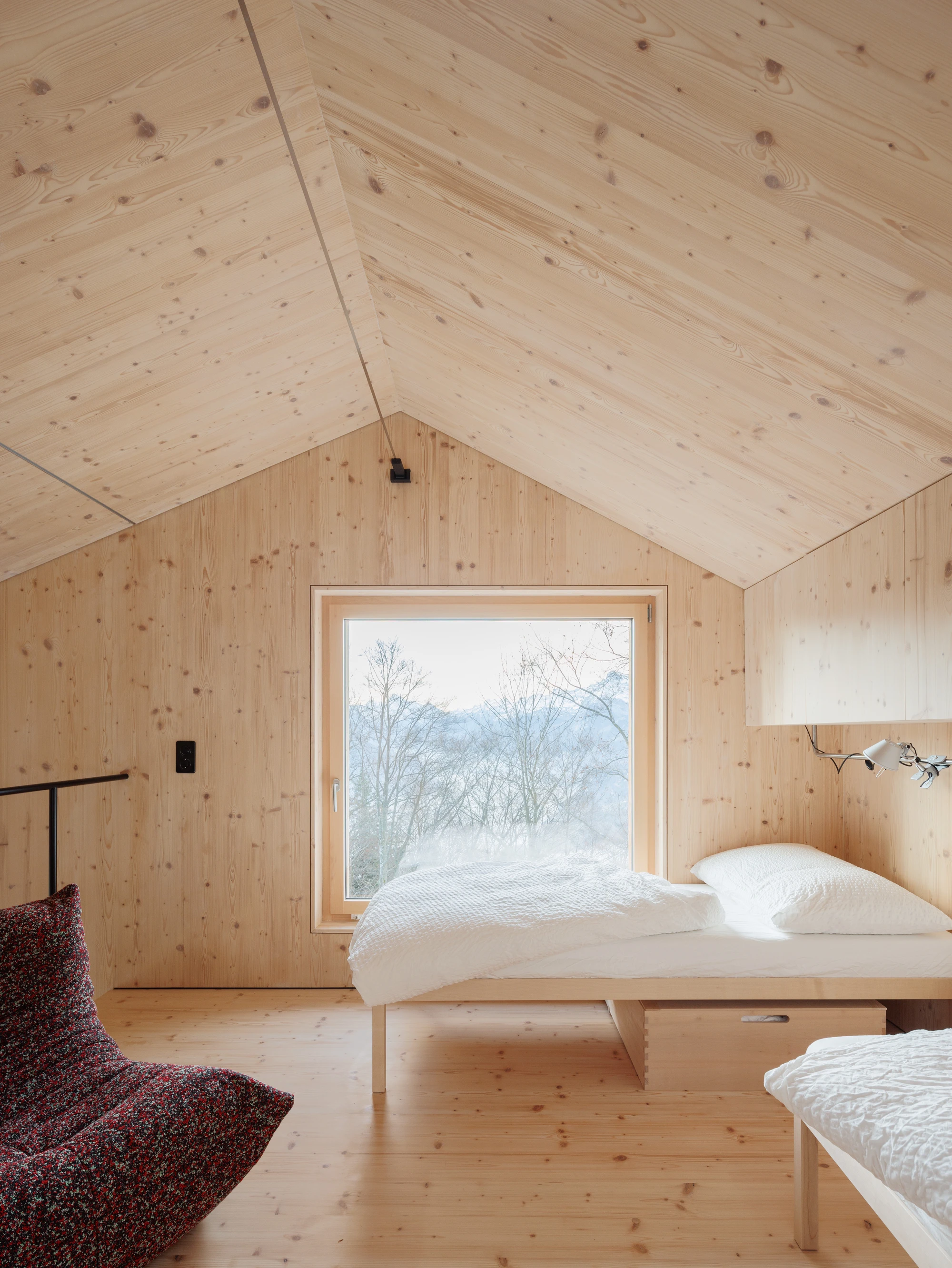 Swiss Alpine Cabin Reconstruction by Guča arch., photographed by Matej Hakár — Exterior side view: the main cabin and the sauna pavilion at the same ridge height, both Corten-trimmed, surrounded by bare-branch winter trees.