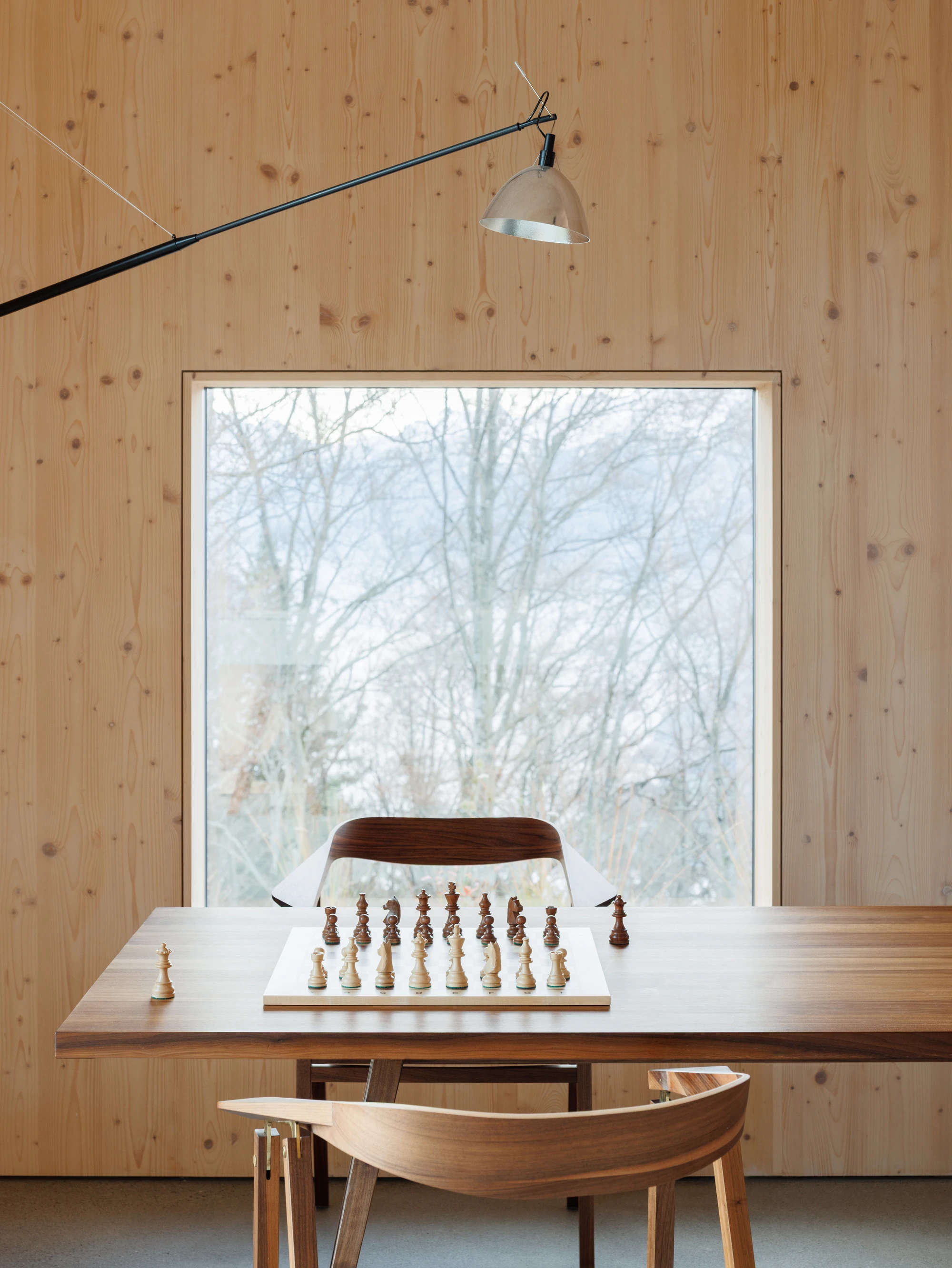 Swiss Alpine Cabin Reconstruction by Guča arch., photographed by Matej Hakár — Interior of the living space looking toward the fireplace sculpture: concrete monolith at centre, the steel stair folded behind it, CLT warm overhead.