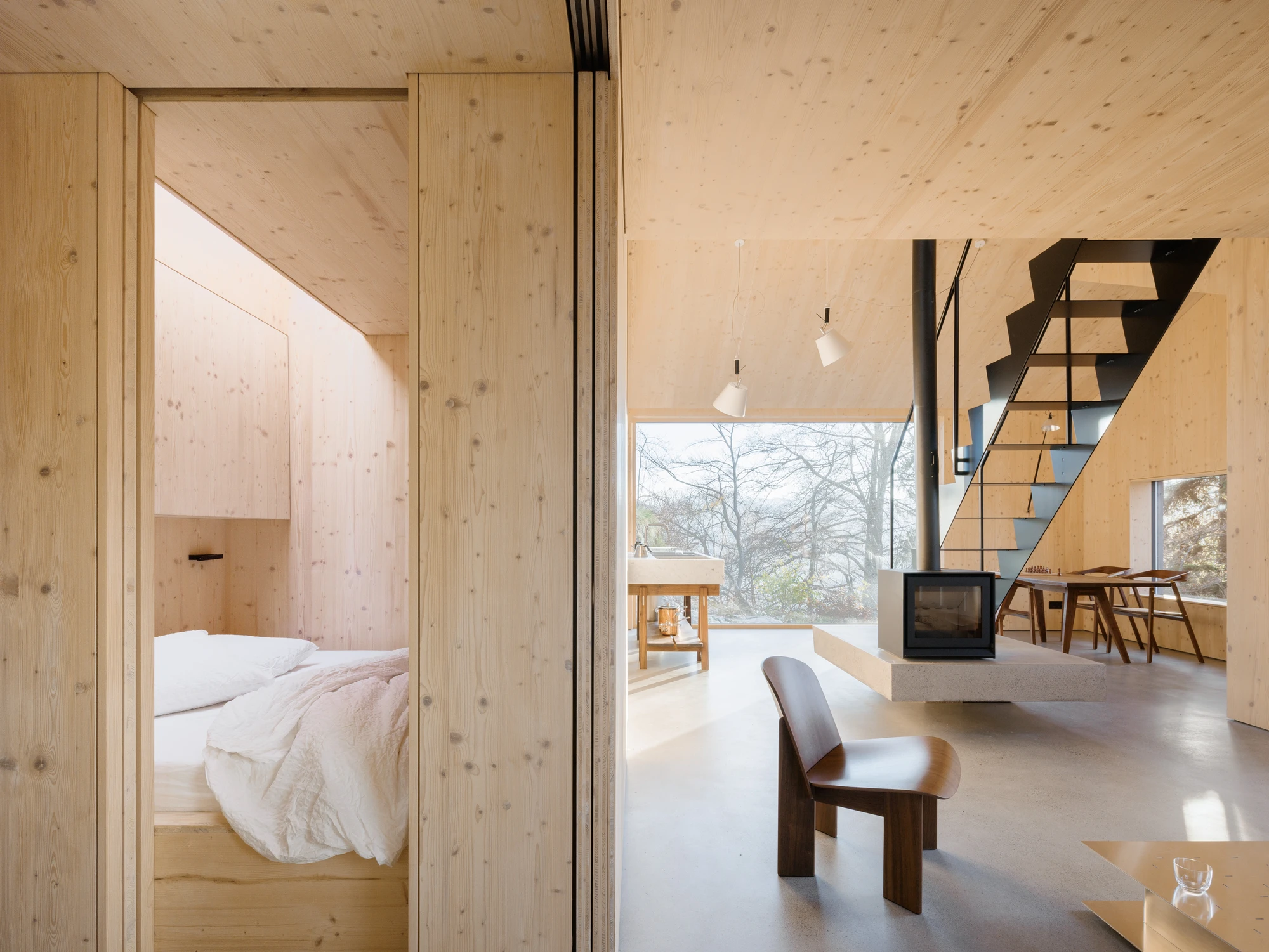 Swiss Alpine Cabin Reconstruction by Guča arch., photographed by Matej Hakár — Interior night view: the living space lit by the fireplace glow, CLT panels reflecting orange-warm light, the black window glass showing the Alpine dark outside.