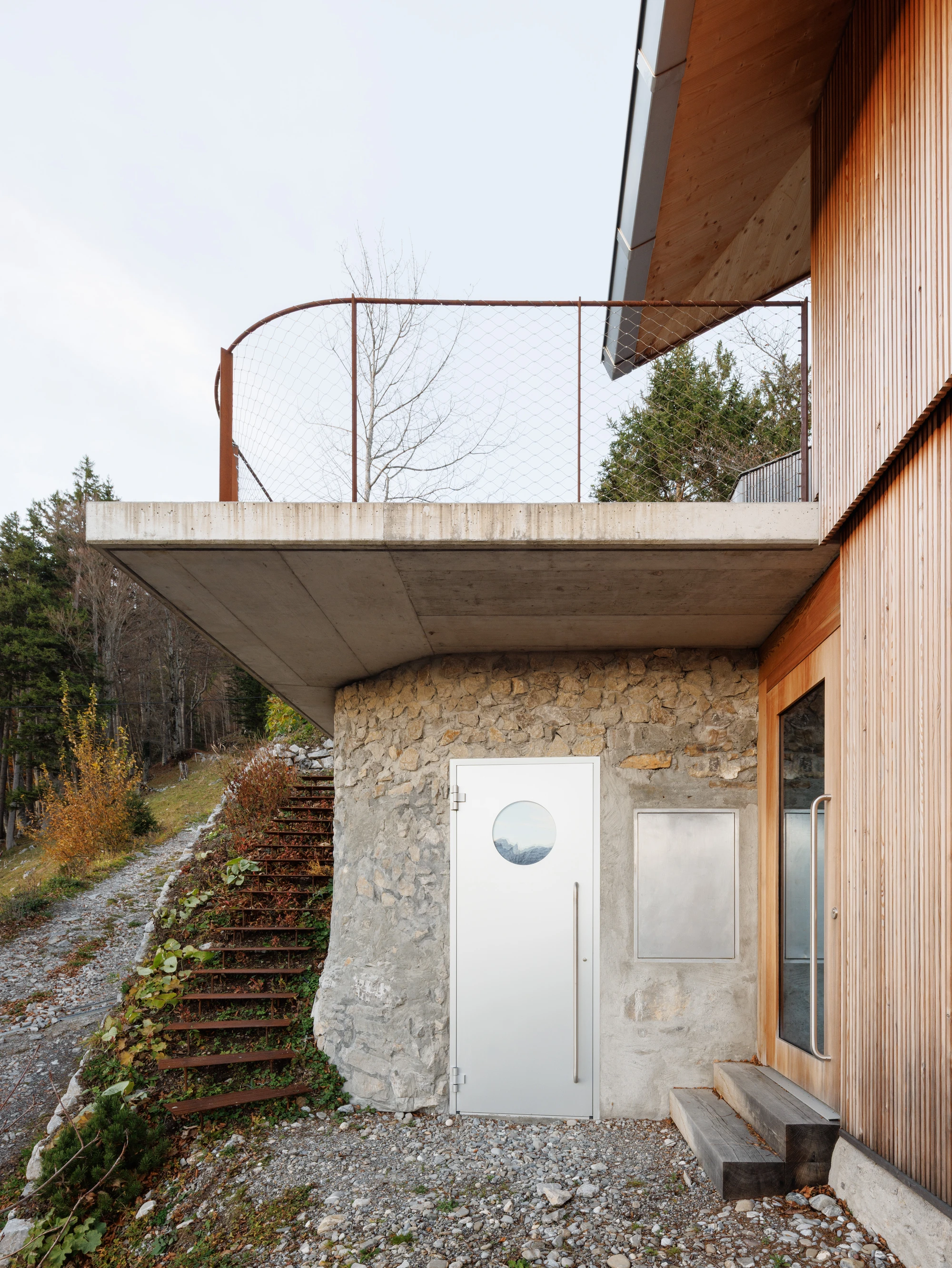 Swiss Alpine Cabin Reconstruction by Guča arch., photographed by Matej Hakár — Interior detail of the CLT staircase zone: light grey exposed CLT panels, black steel stair treads, a single pendant light hanging from the wood ceiling.