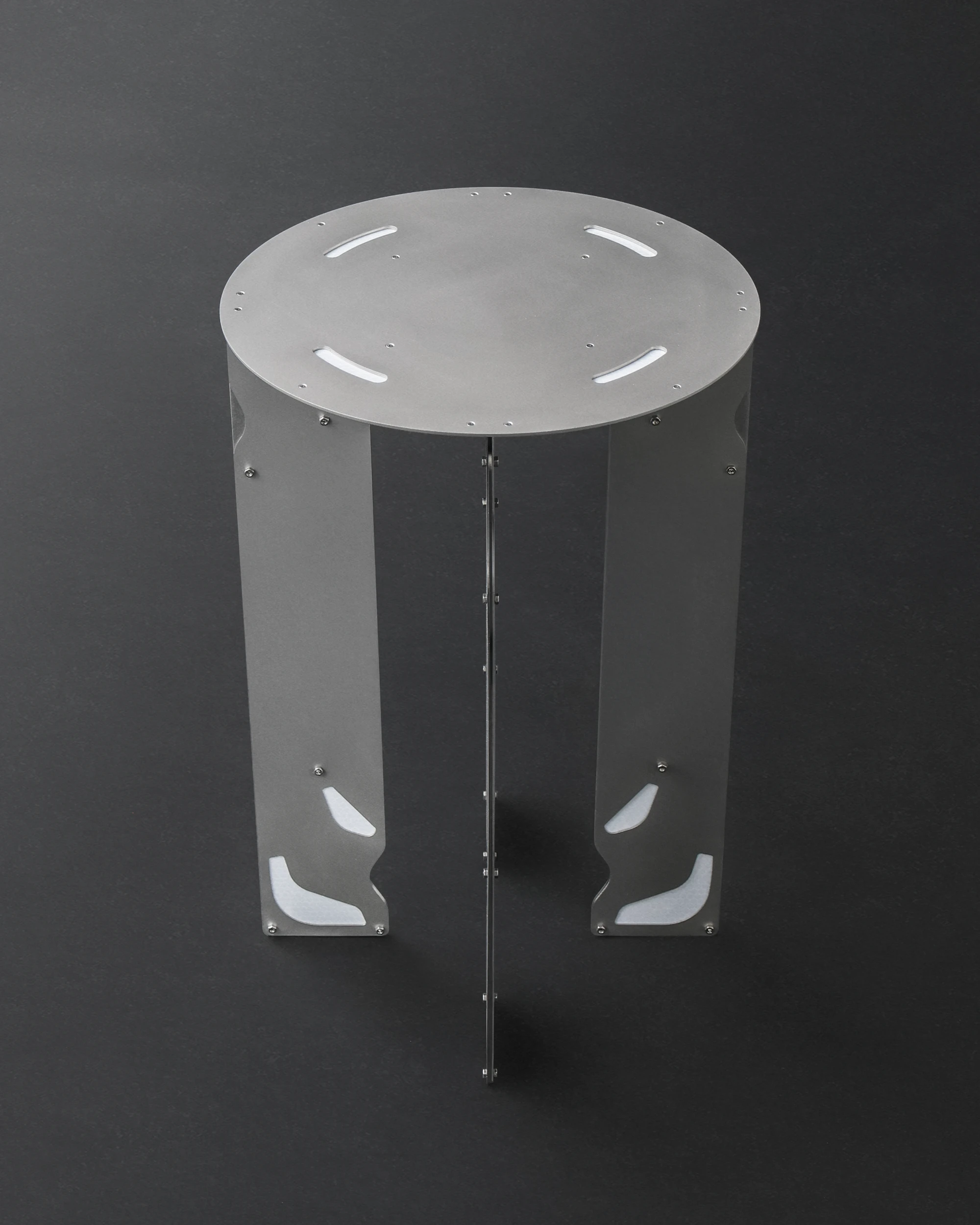 Retroreflective Stool by A POW STUDIO, photographed by hyunbeom Lee — Overhead view of the retroreflective stool top: the circular matt surface with reflective trim catching the light, bolt pattern visible at the junctions.